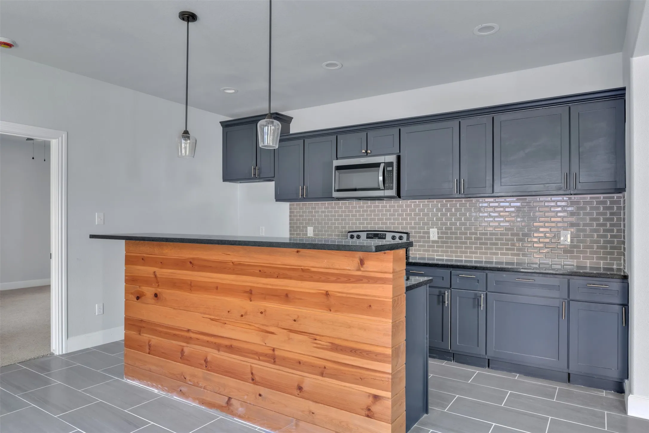 Kitchenette featuring dark gray cabinetry, stainless steel microwave, and subway tile backsplash