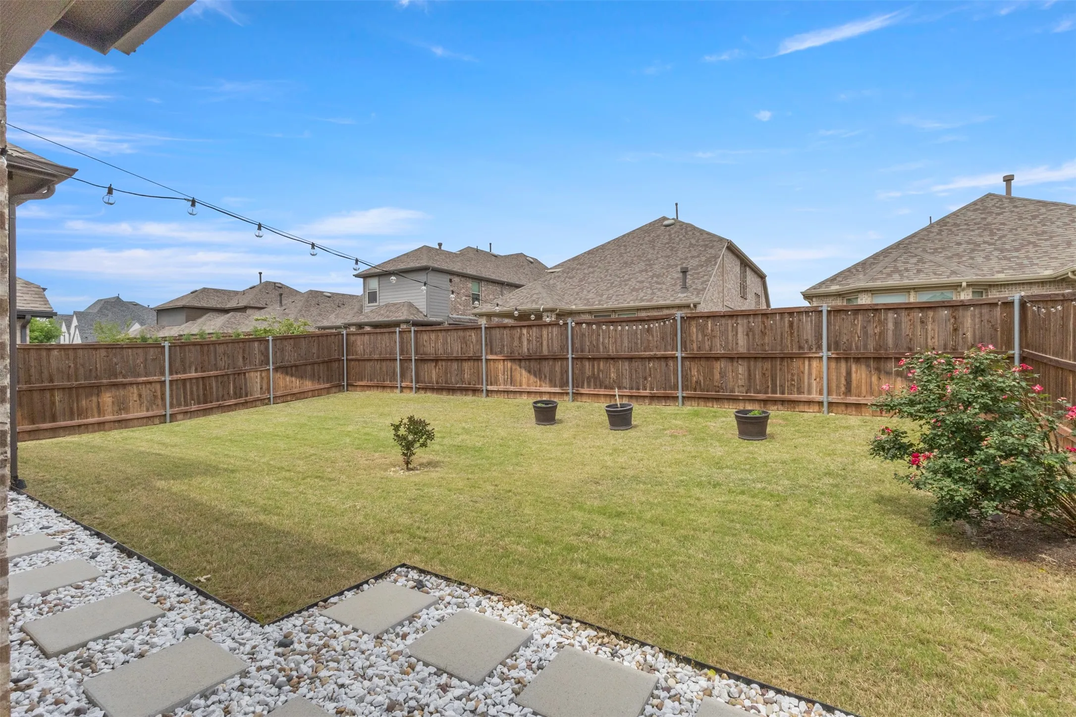 Manicured backyard featuring a privacy fence, lush lawn, and stone paver patio area