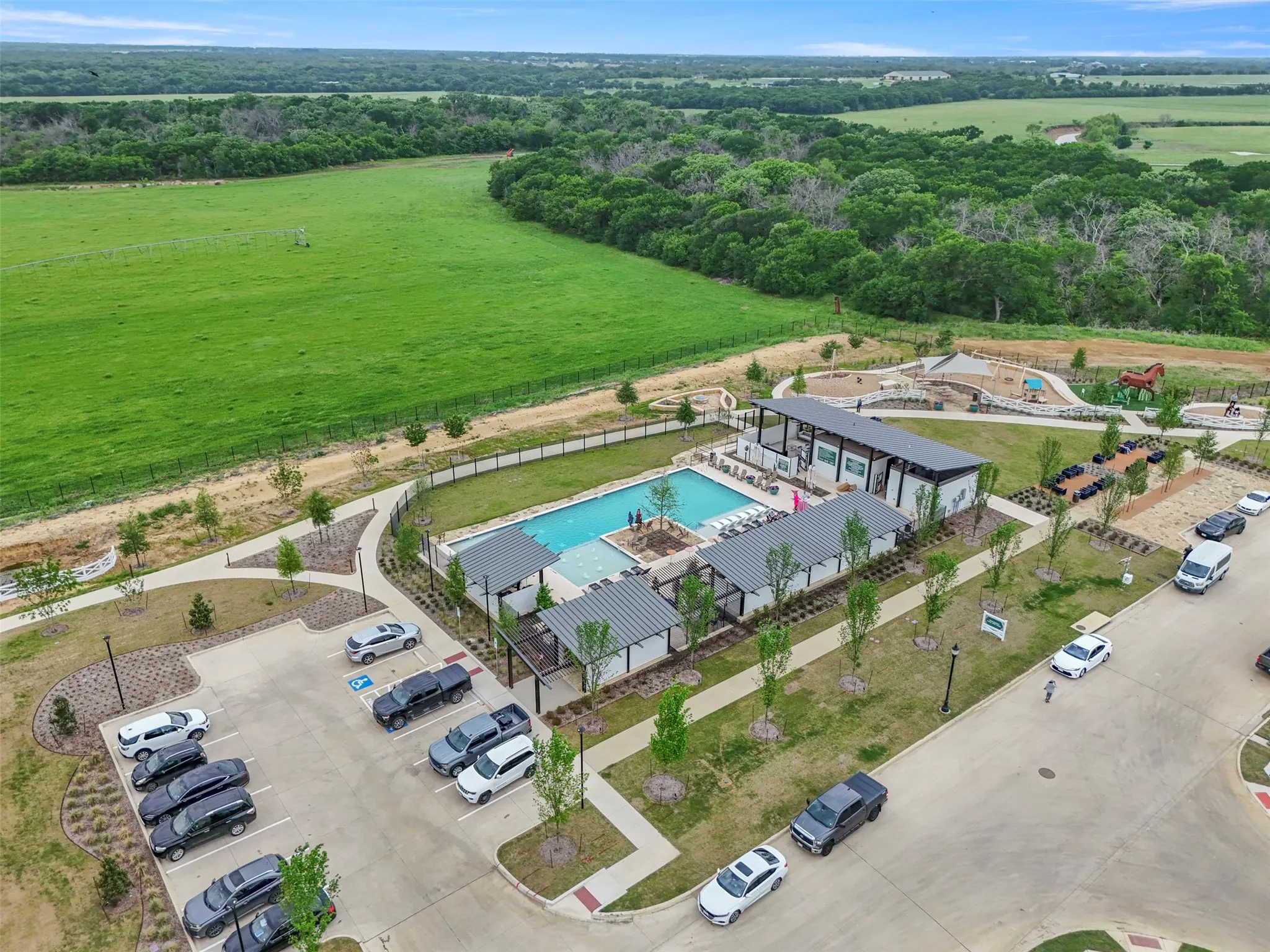 Community pool area featuring a large swimming pool, two covered patio structures, and a playground with a custom Horse play area for the kids and a firepit for the adults
