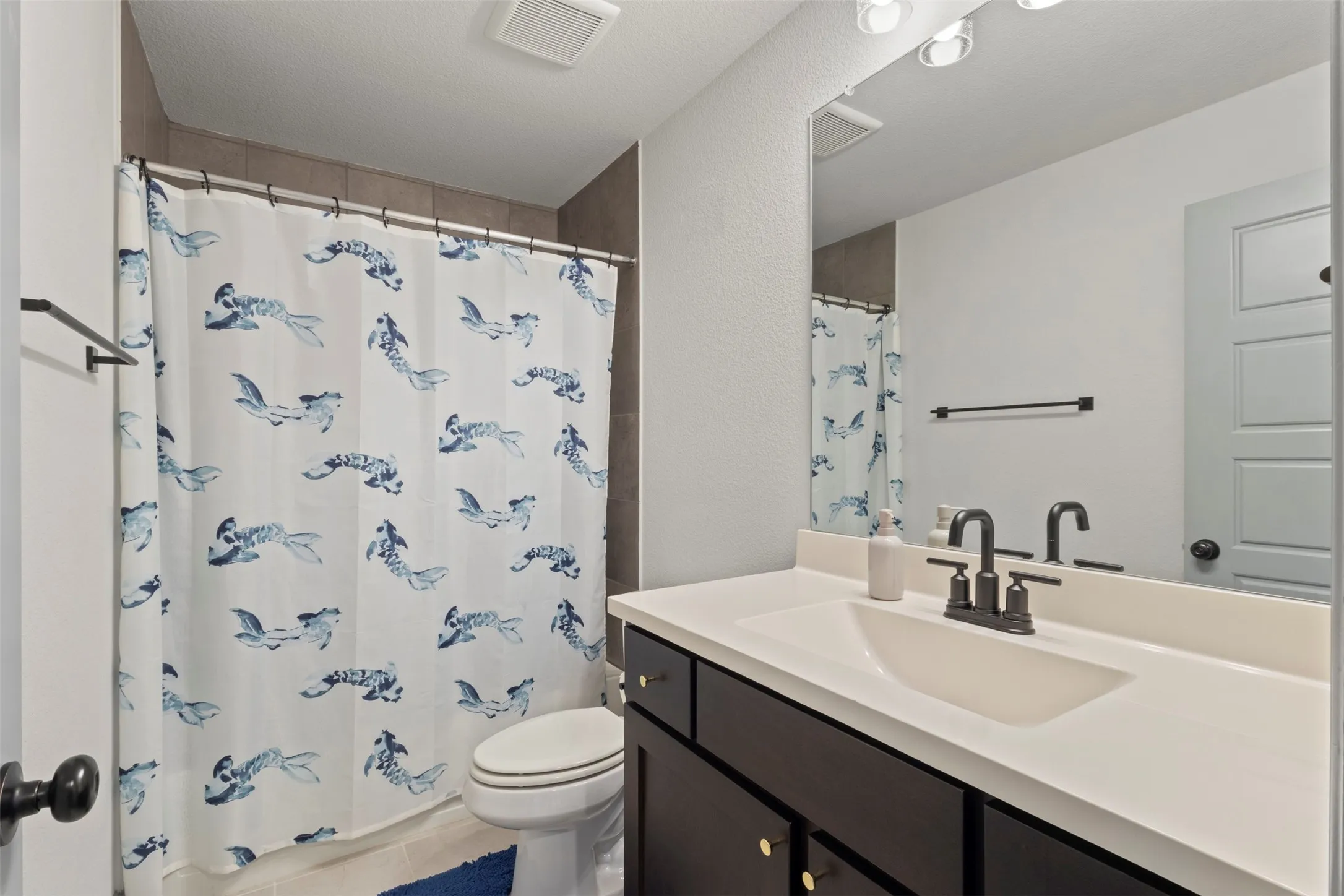 Bathroom featuring a dark wood-finish vanity with a white integrated sink, matte black faucet, and a large wall-mounted mirror