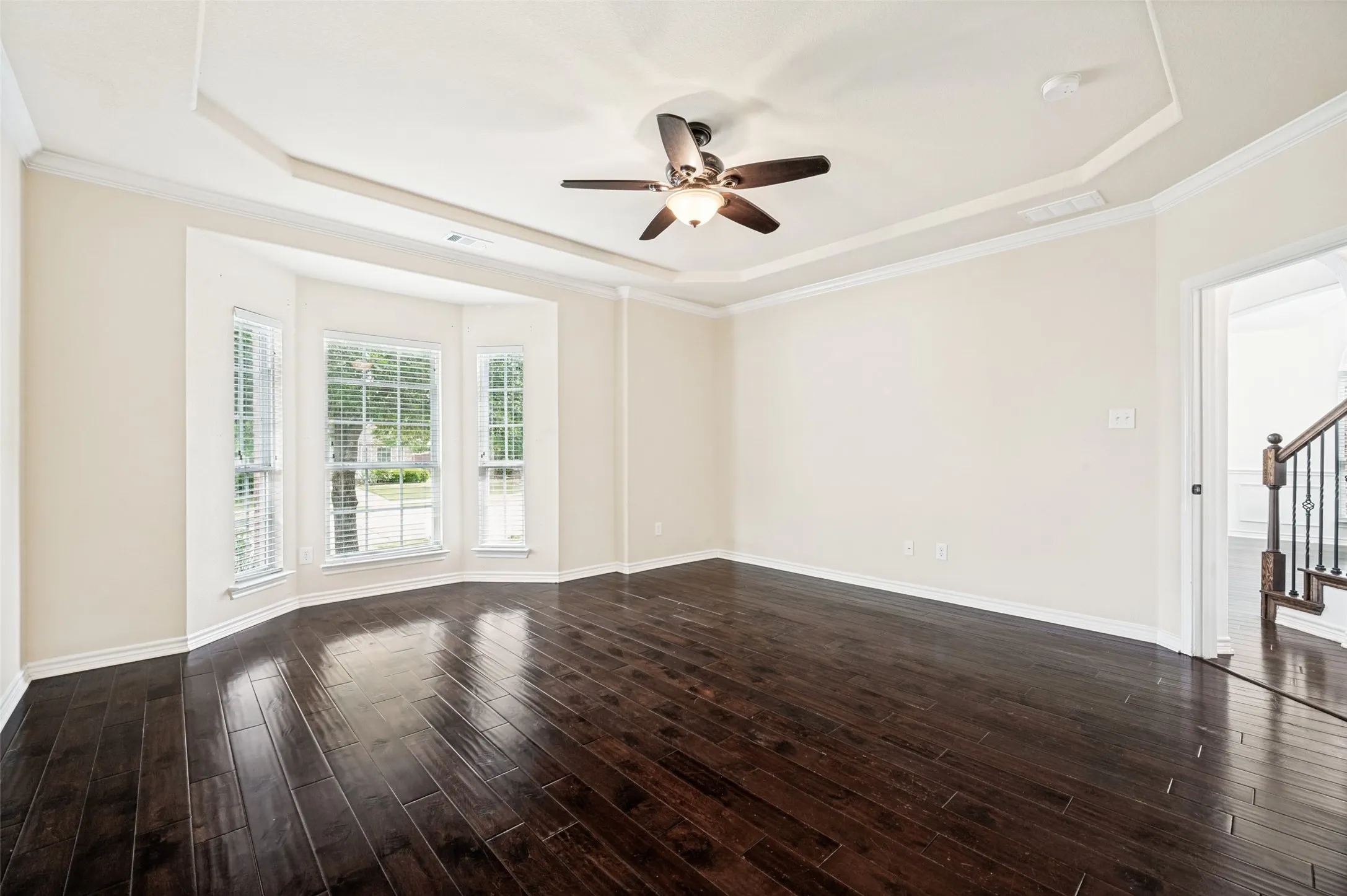 Spacious Primary Bedroom featuring dark wood-finish flooring, a tray ceiling with crown molding, and a ceiling fan