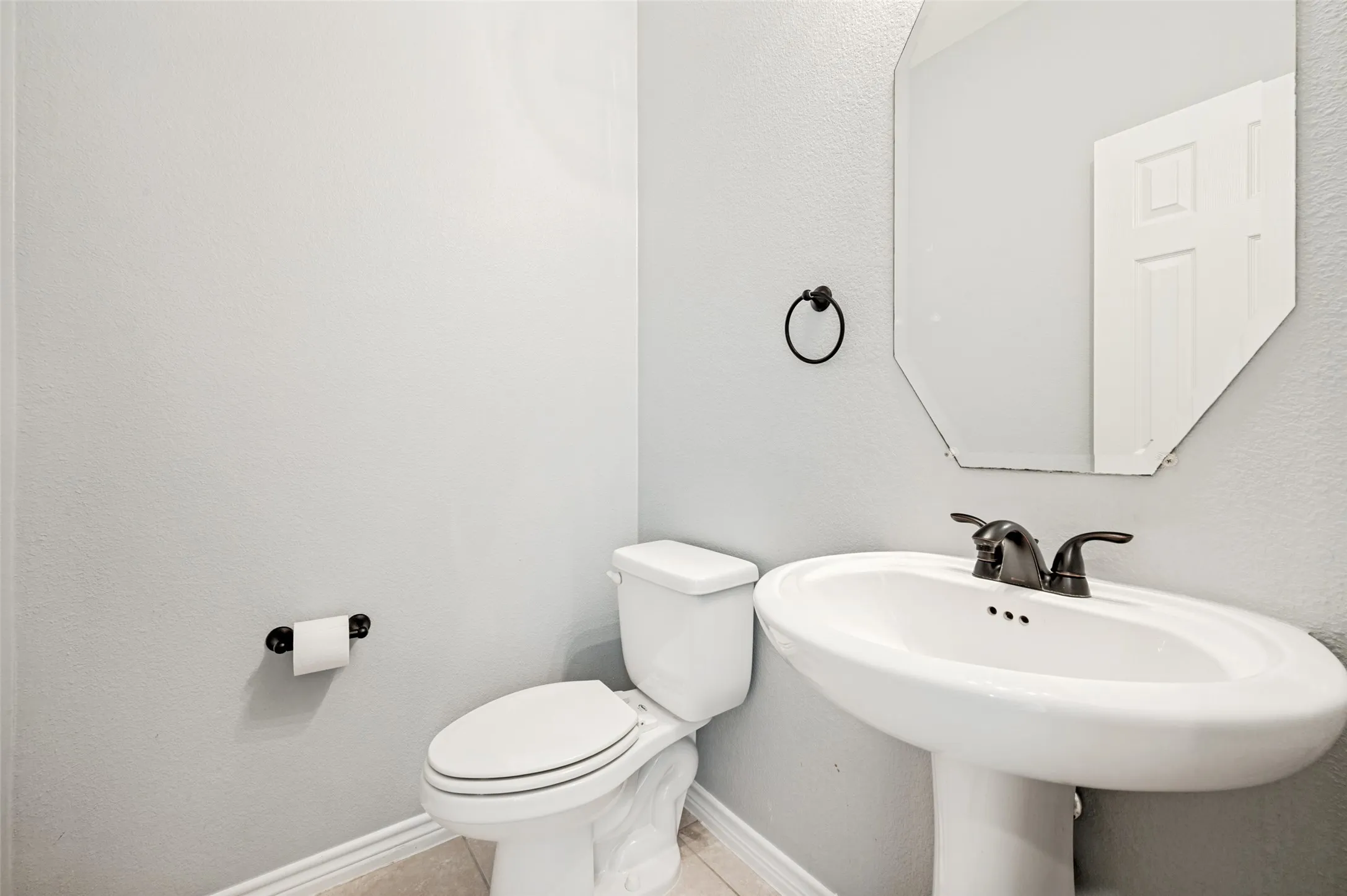 Half bathroom with Pedestal sink with oil-rubbed bronze fixtures, an octagonal mirror, and light-toned wall paint