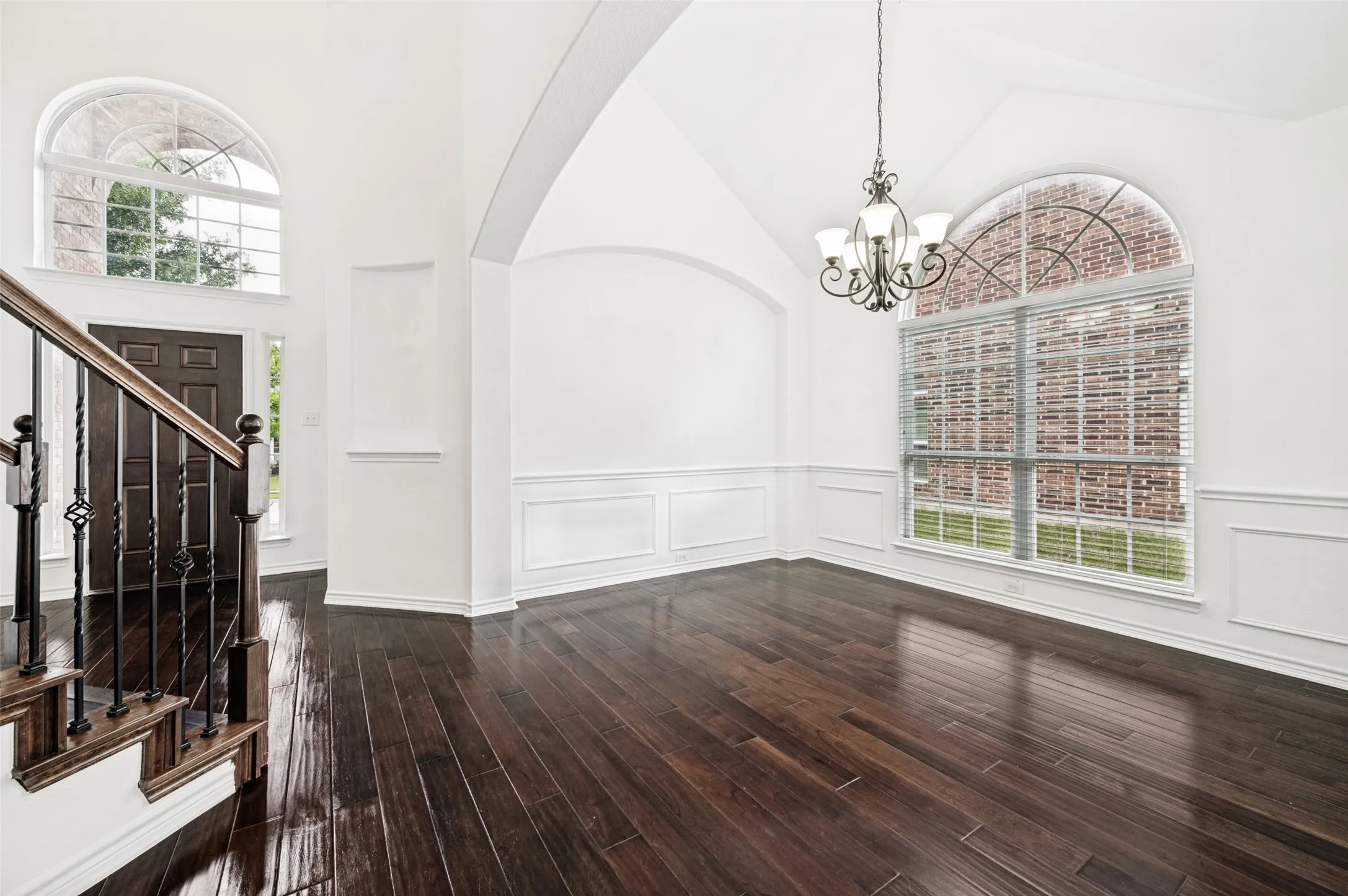Entry and room featuring dark wood-finish flooring, tall vaulted ceilings, arched doorways, wainscoting, and large arched windows with blinds