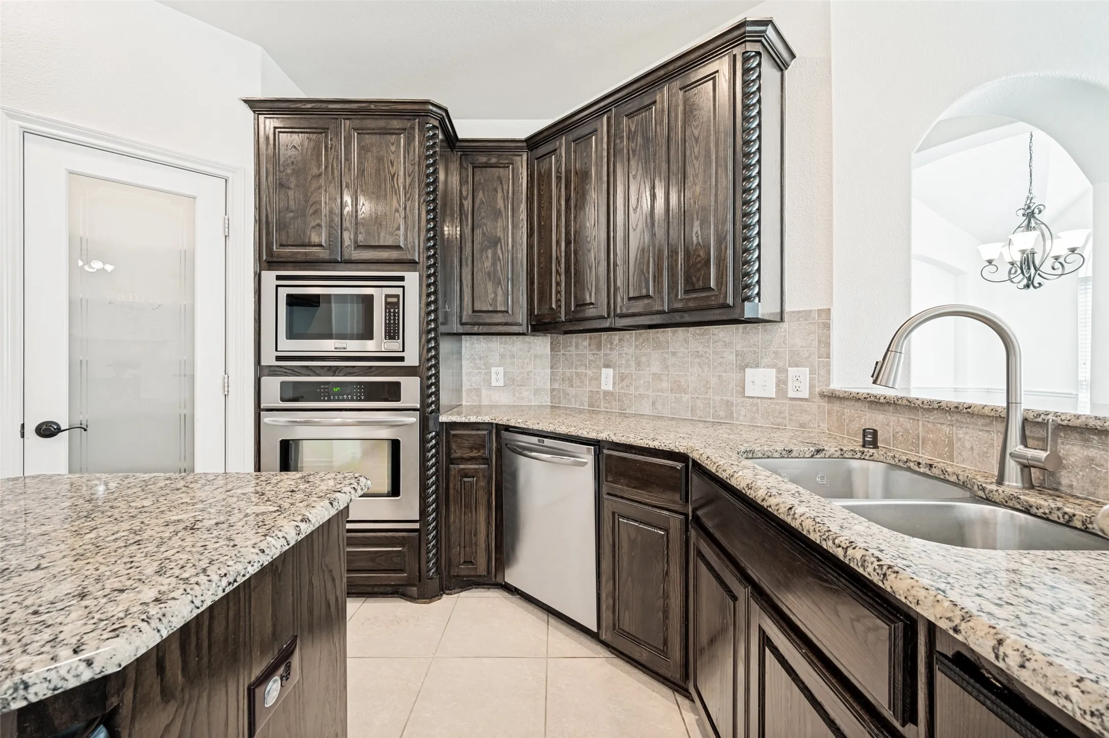 Kitchen featuring dark wood cabinetry, light granite countertops, stainless steel appliances, and a tiled backsplash