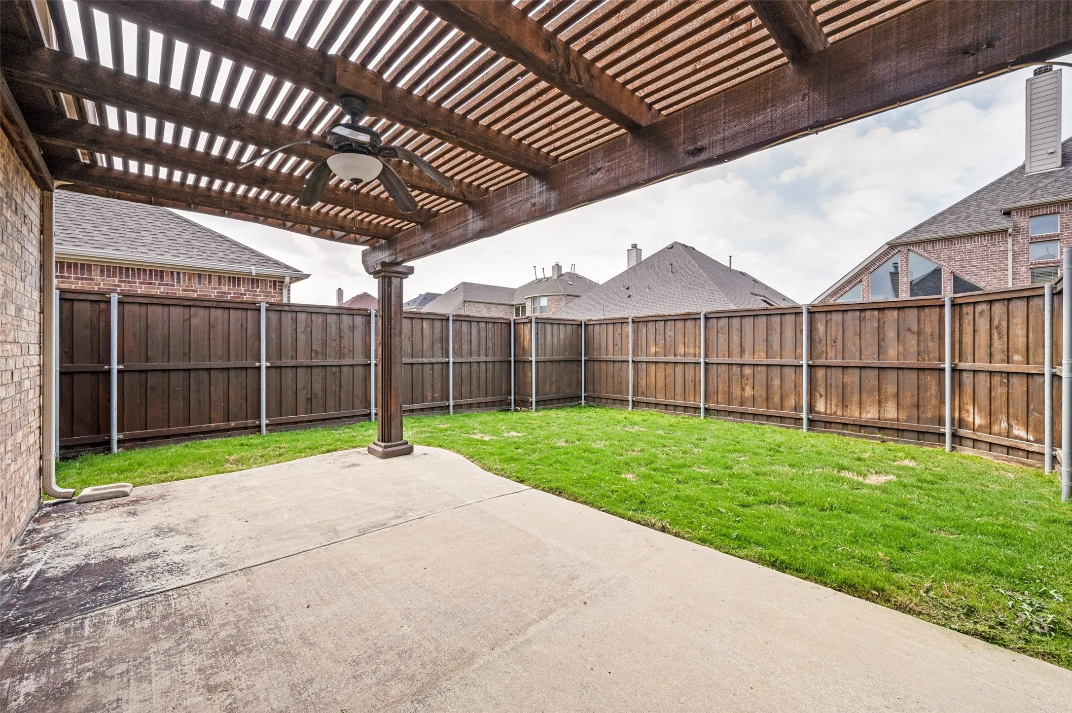 Patio space featuring a wood pergola with ceiling fan, privacy fencing, a concrete pad, and a grass area