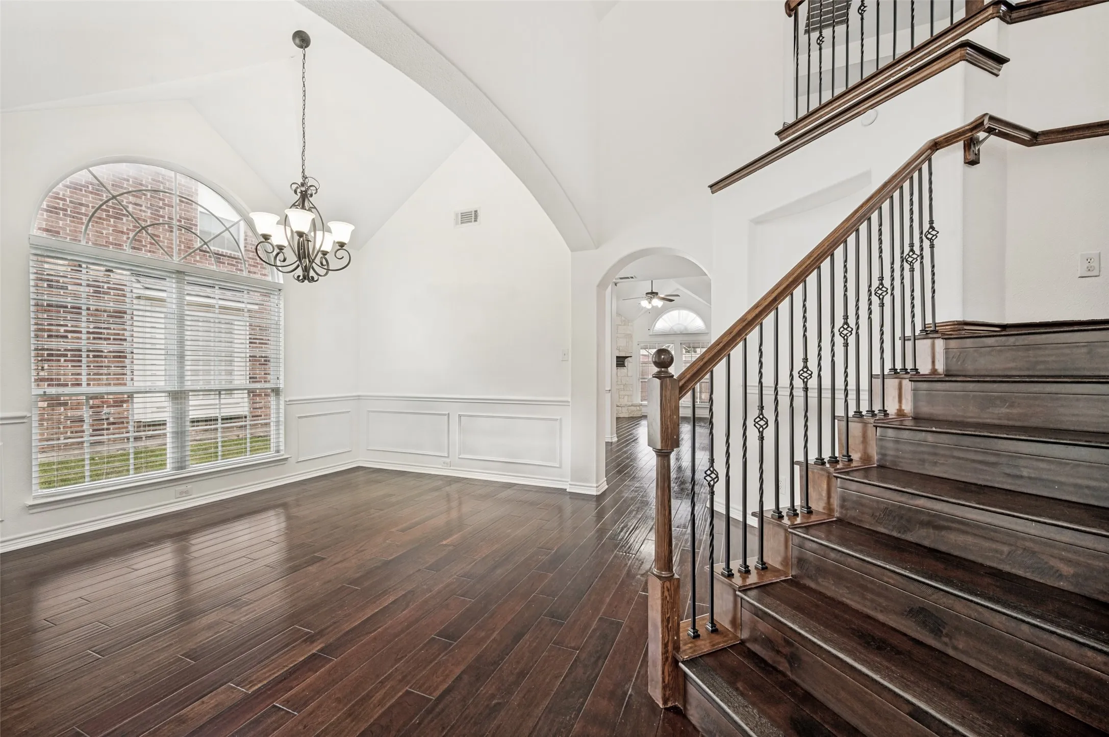 Formal dining area featuring vaulted ceilings, wood-finish flooring, wainscoting, and an arched window with blinds
