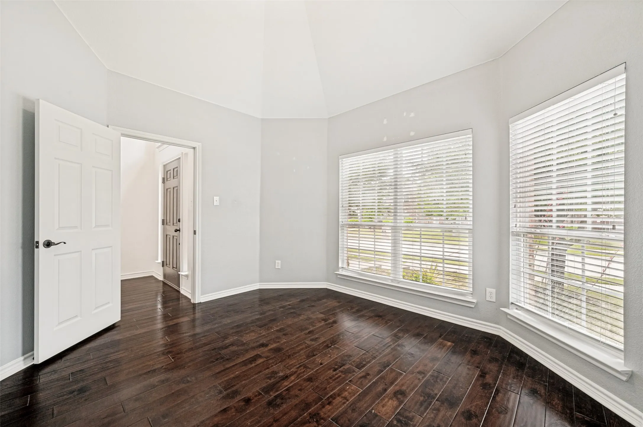 Room featuring dark wood-finish flooring, vaulted ceilings, and light-toned walls