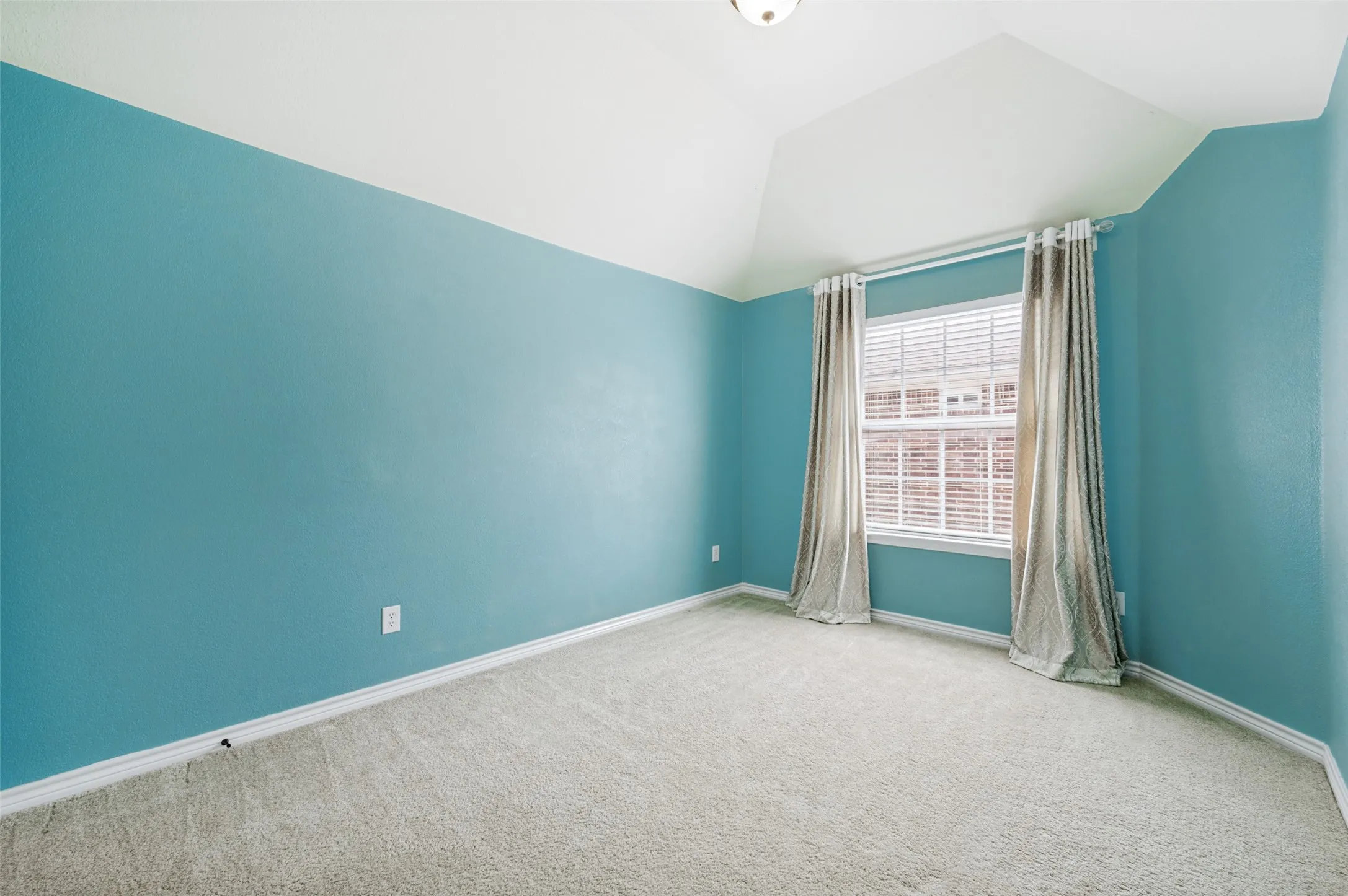 Spacious room featuring vaulted ceilings, a large window with blinds, light-colored carpeting, and teal-painted walls with white trim