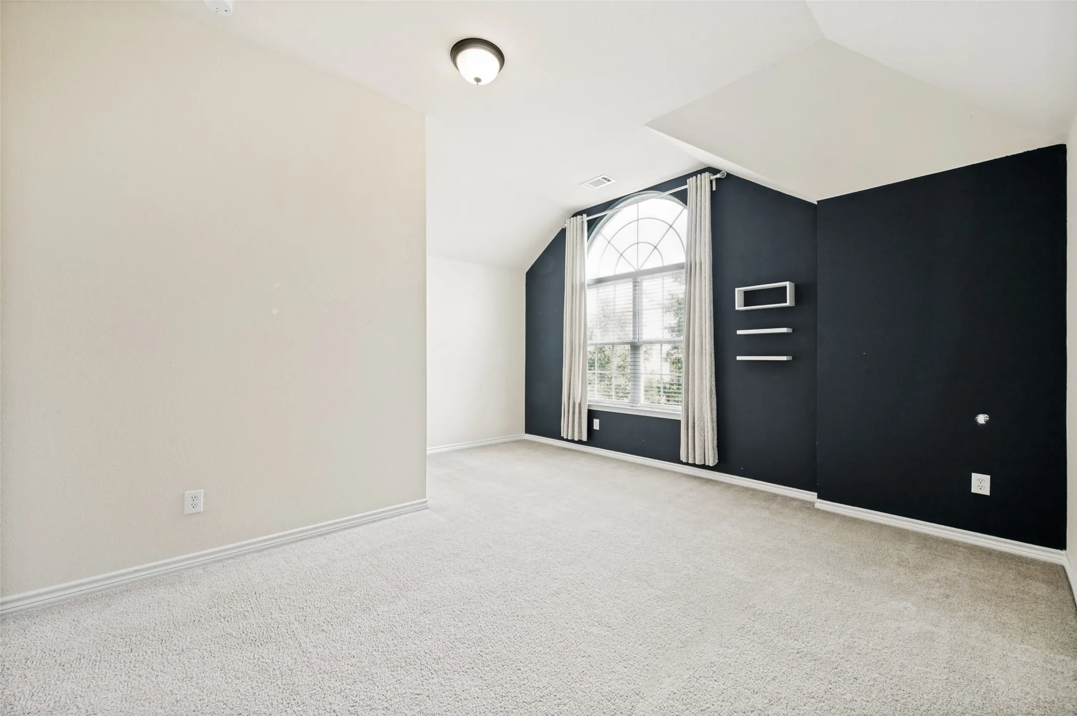 Bedroom featuring an arched window, soft carpeting, and a dark accent wall