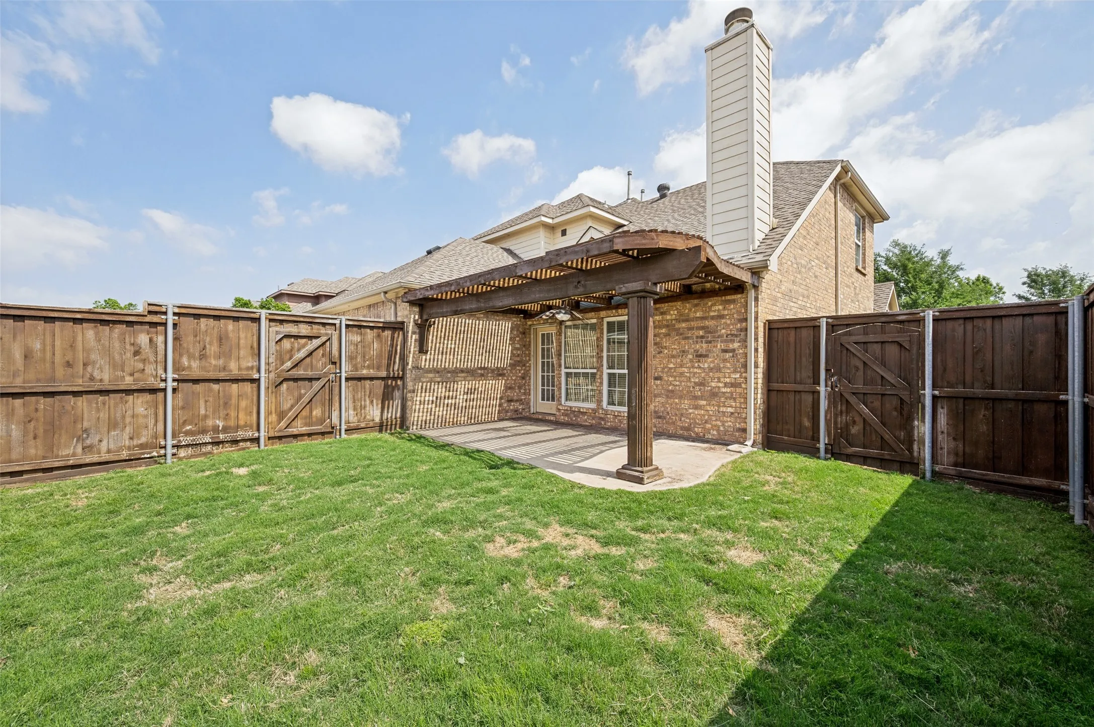 Fenced backyard featuring a pergola-covered patio, brick exterior, and a manicured lawn