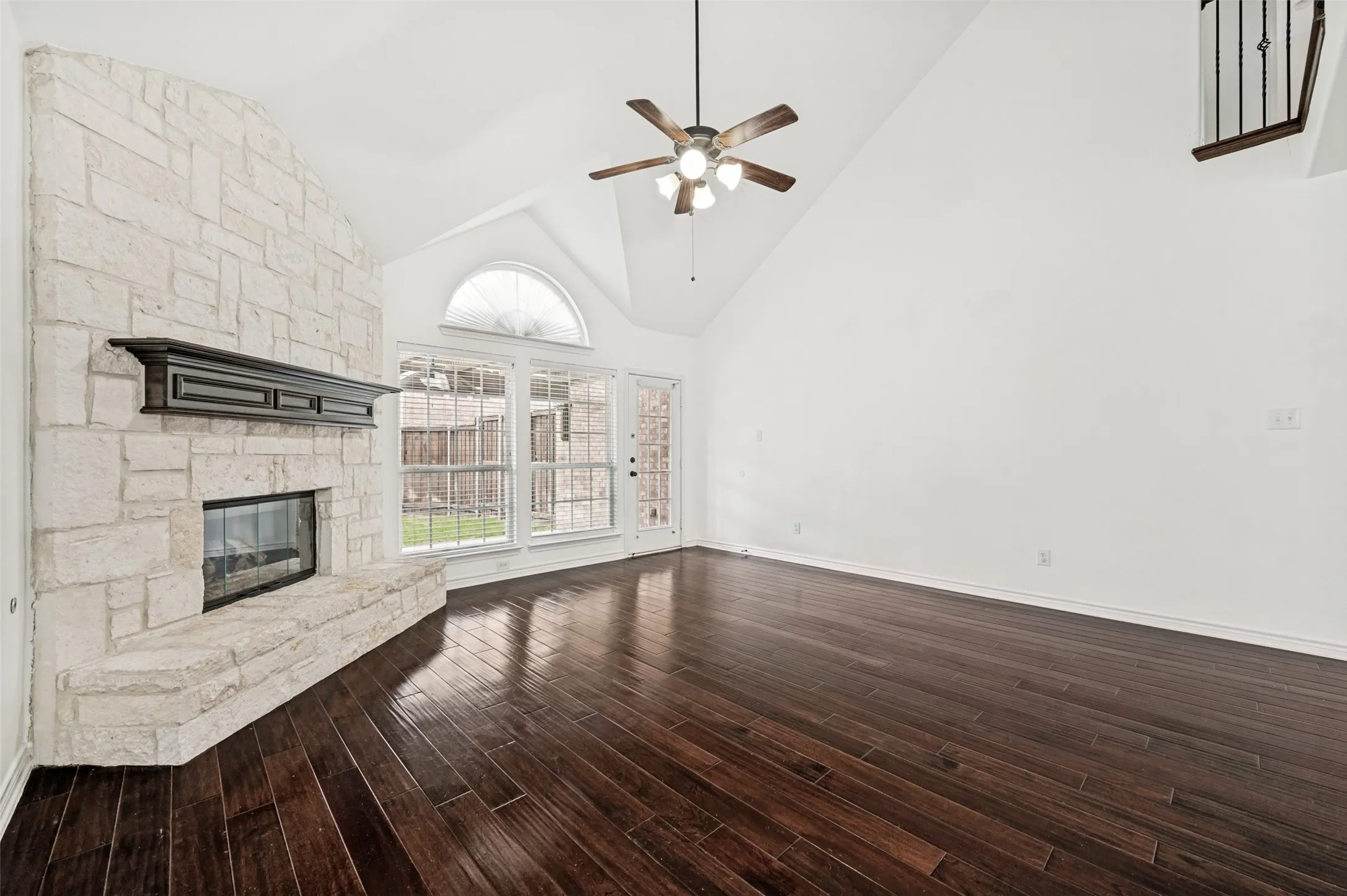 Spacious living area featuring a stone fireplace with a dark wood mantel, high vaulted ceilings, and dark wood-finish flooring