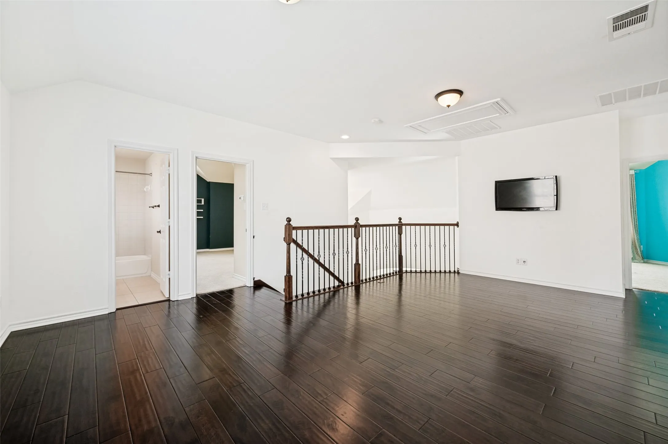 Expansive loft space with dark wood-finish flooring, white walls, and a vaulted ceiling