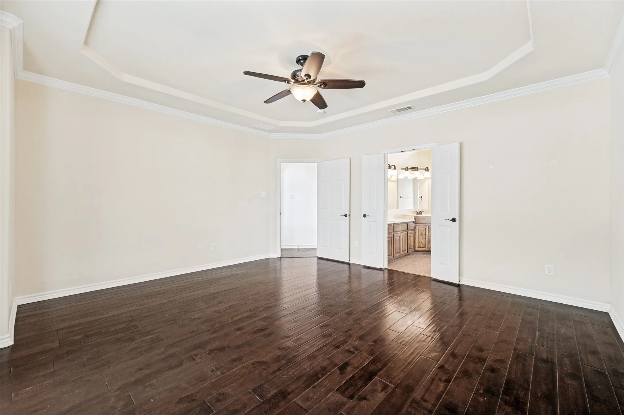Spacious Primary Bedroom featuring wood-finish flooring, a tray ceiling, and a ceiling fan with integrated lighting