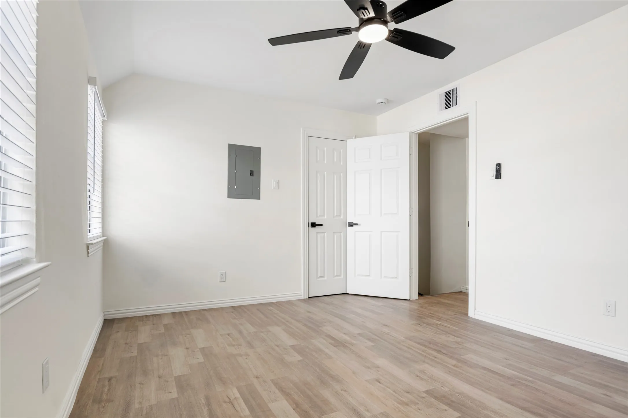 Room featuring light wood-finish flooring, white painted walls, and a black ceiling fan with integrated lighting