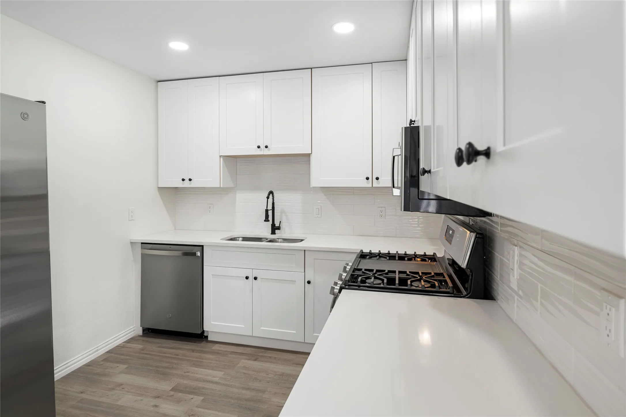Contemporary kitchen featuring white shaker cabinetry, quartz countertops, subway tile backsplash, stainless steel appliances, and wood-finish flooring