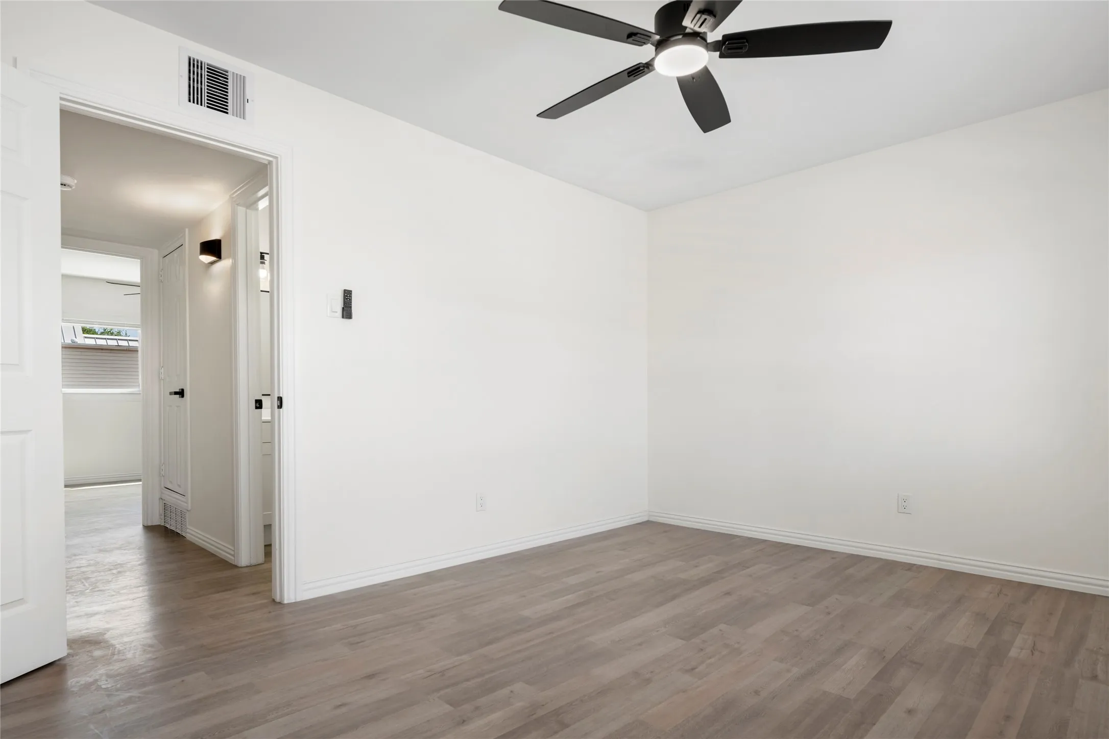 Spacious room featuring wood-finish flooring, crisp white walls, a modern ceiling fan with integrated lighting, and white baseboards
