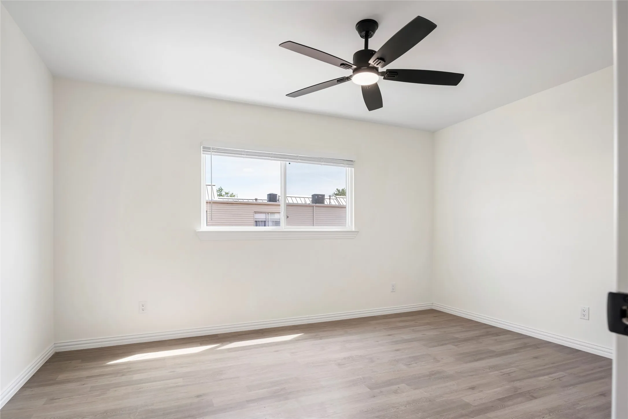 Bright room featuring a window with white blinds, wood-finish flooring, a ceiling fan with integrated lighting, white walls, and white trim