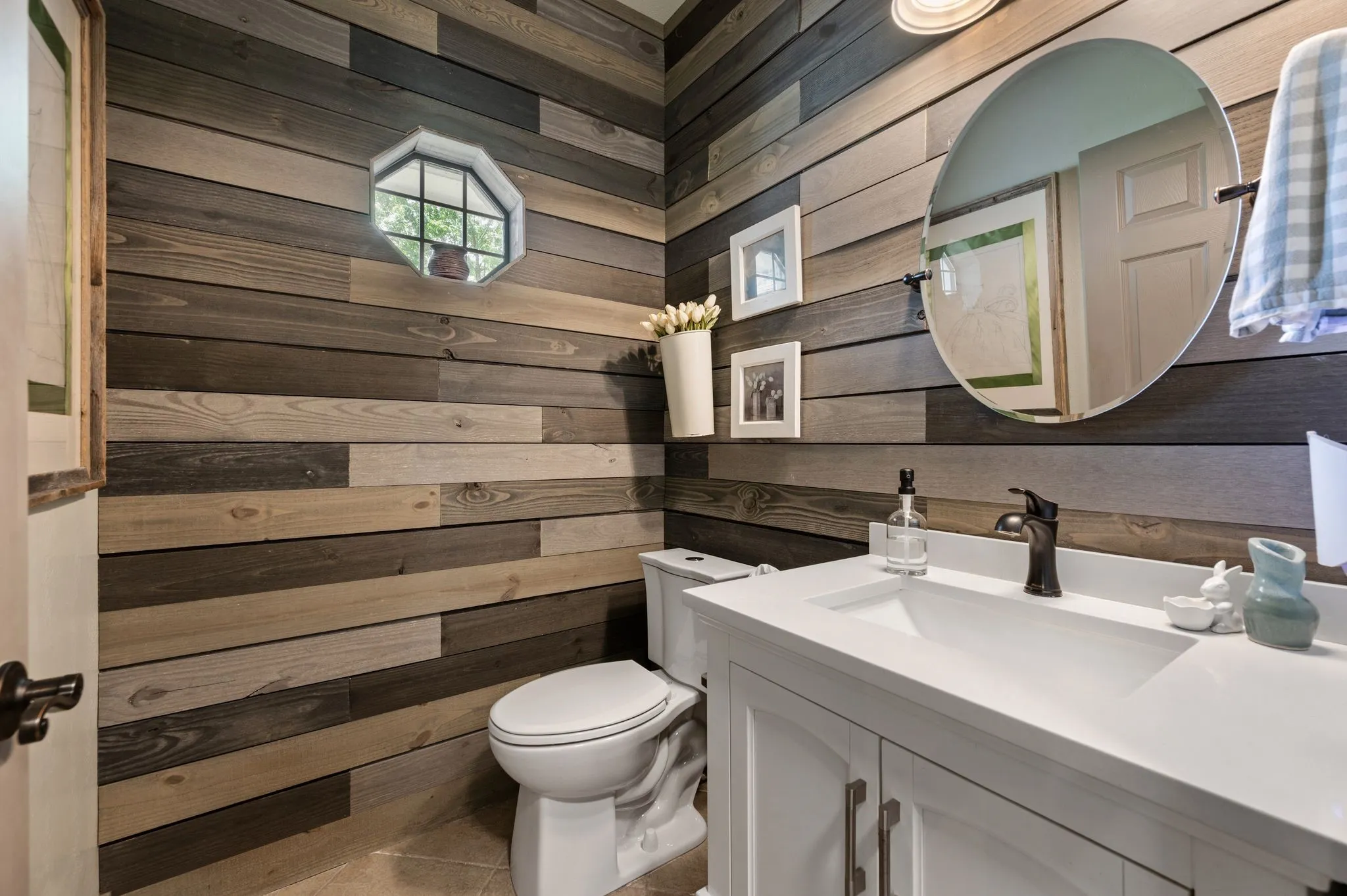 The downstairs half bath includes shiplap walls, a quarter topped vanity with under mount sink, a dual flush elongated toilet, tile flooring and farmhouse fixtures and hardware.