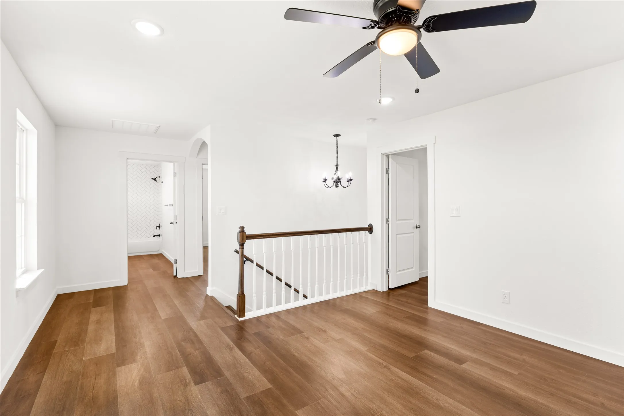 Open upper landing with wood-finish flooring, white balustrade with wood handrail, and recessed lighting