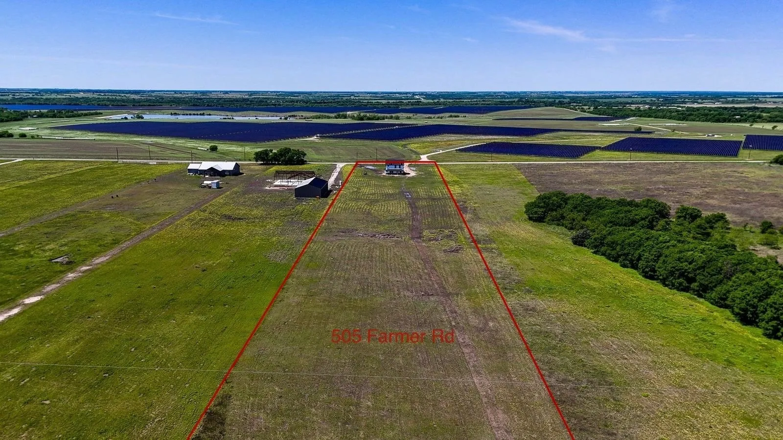 Expansive agricultural land featuring a white single-story home with a red roof, multiple outbuildings, and mature trees