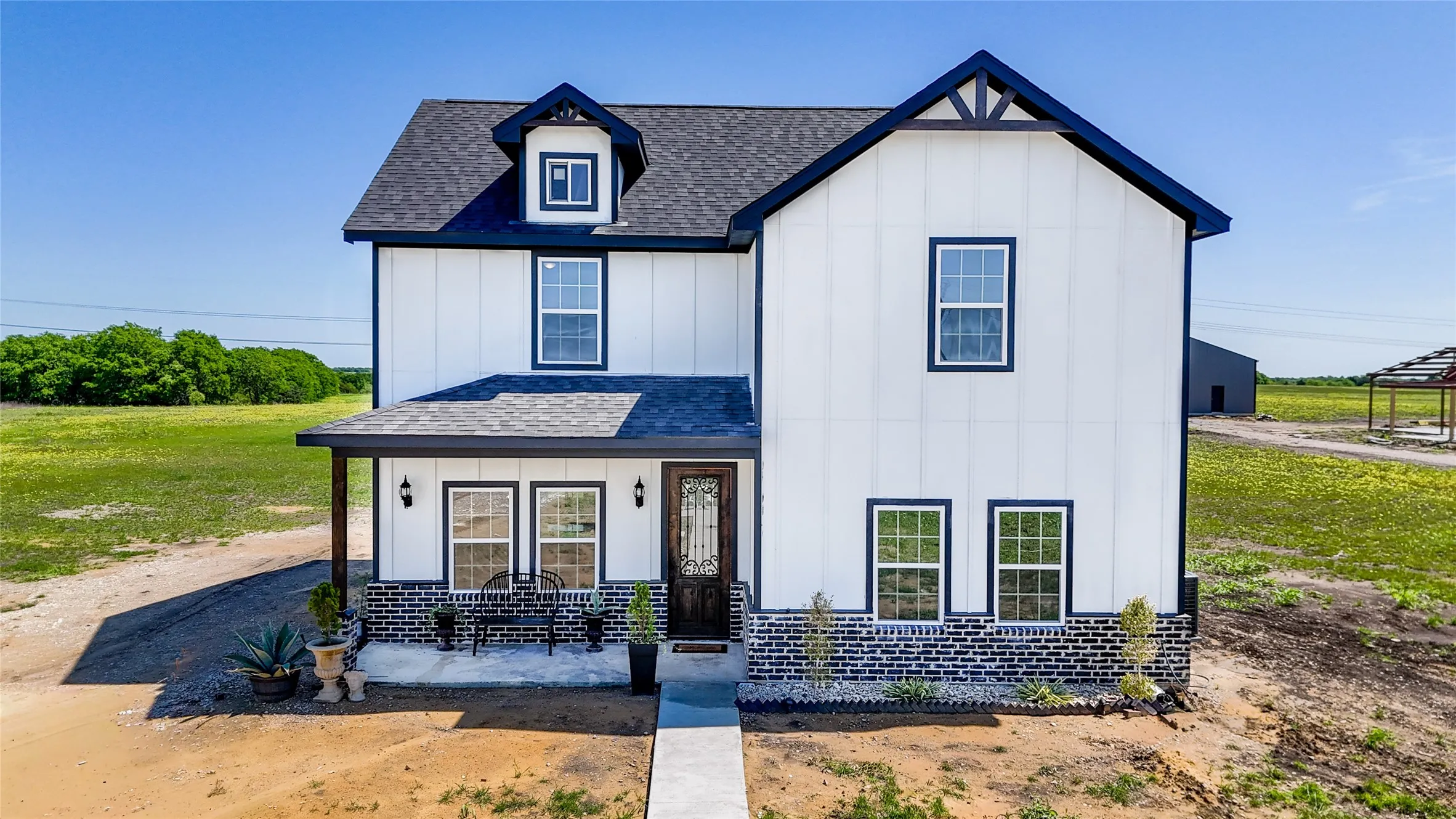 Modern farmhouse exterior featuring white vertical siding with dark trim, a dark shingle roof, a covered front porch, and a dormer window