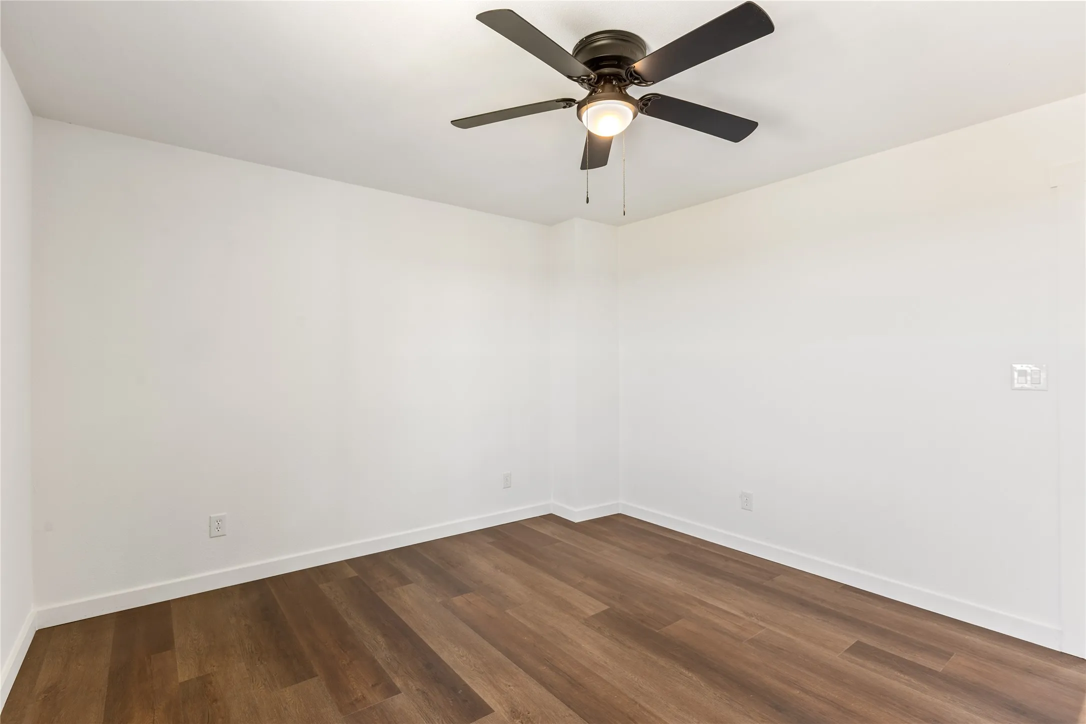 Room featuring wood-finish flooring, white baseboards, and a ceiling fan with integrated lighting