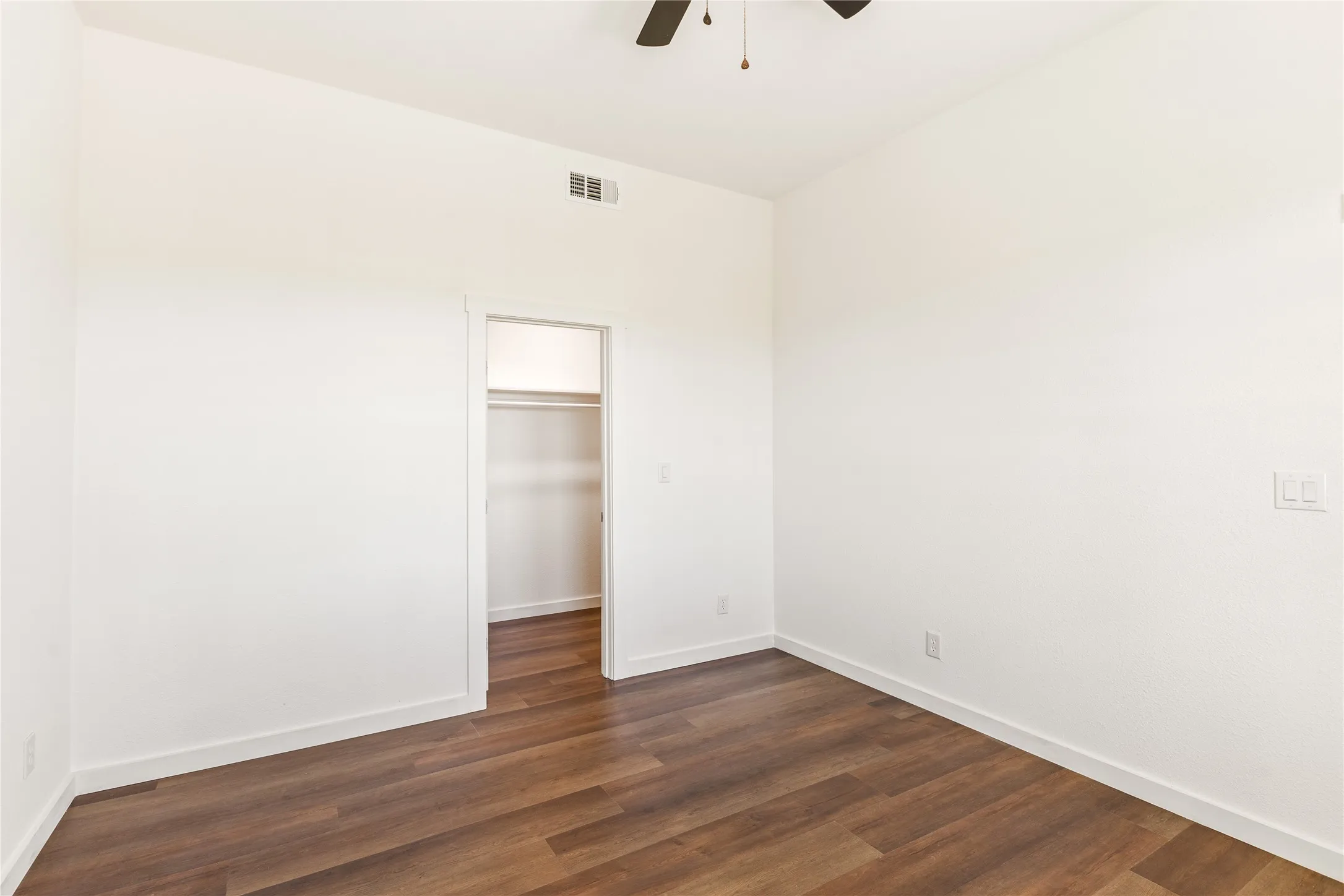 Room featuring wood-finish flooring, white walls, and a ceiling fan