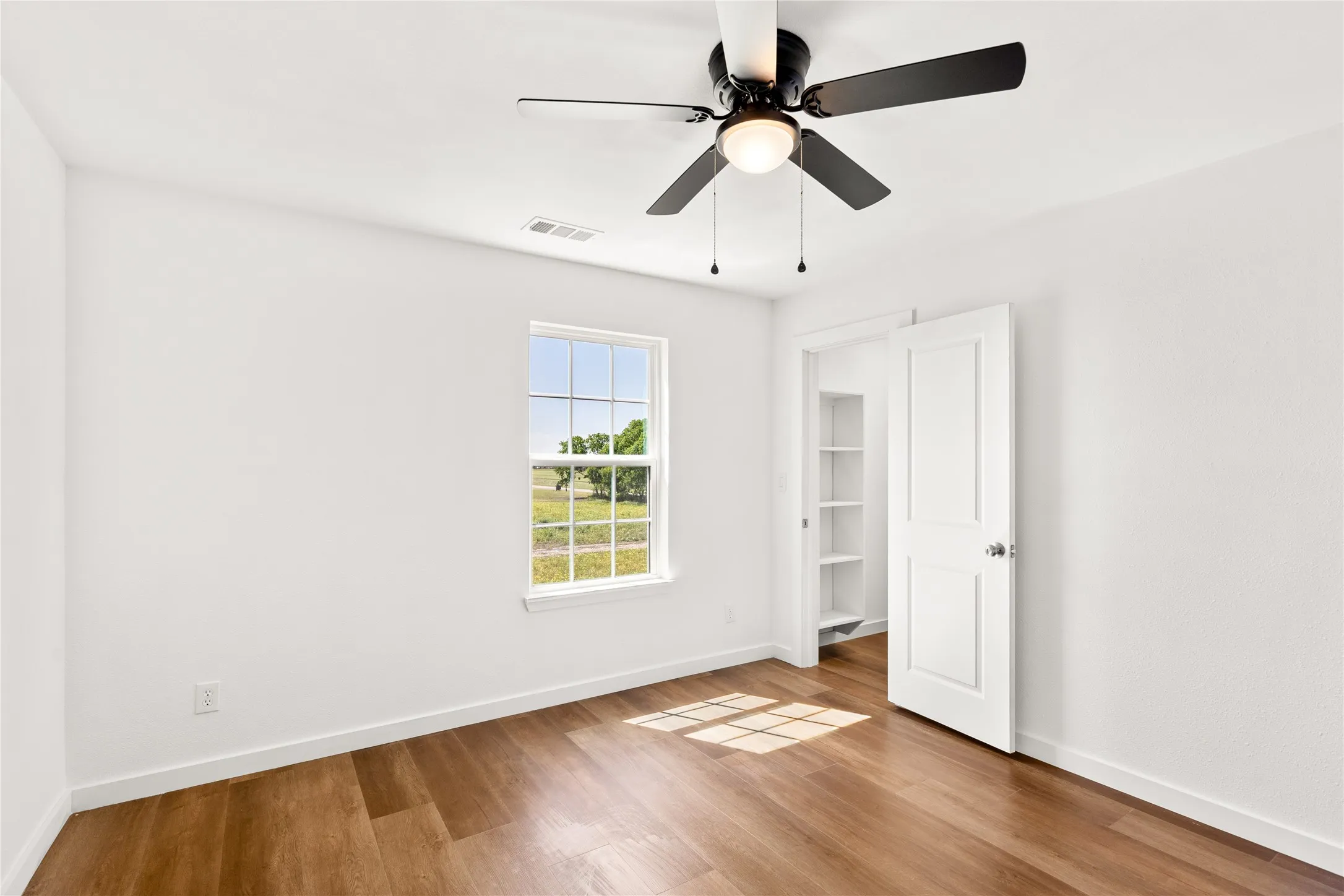 Bright interior space featuring wood-finish flooring, white walls, and a ceiling fan with integrated lighting