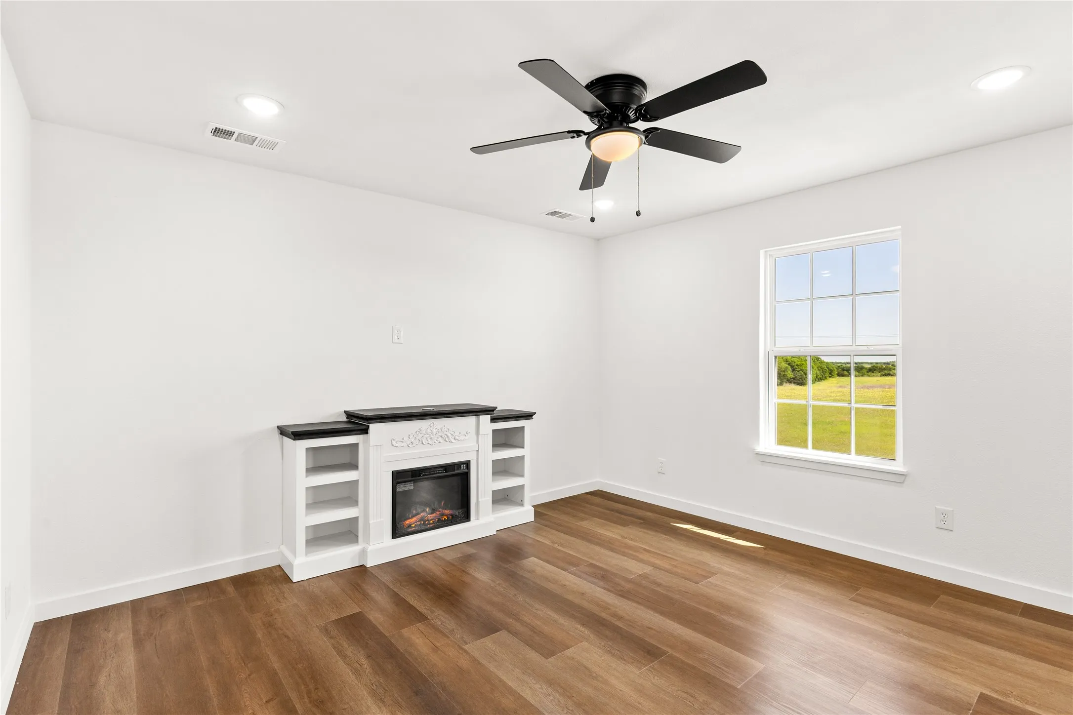 Spacious room featuring wood-finish flooring, a ceiling fan with integrated lighting, and recessed ceiling lights