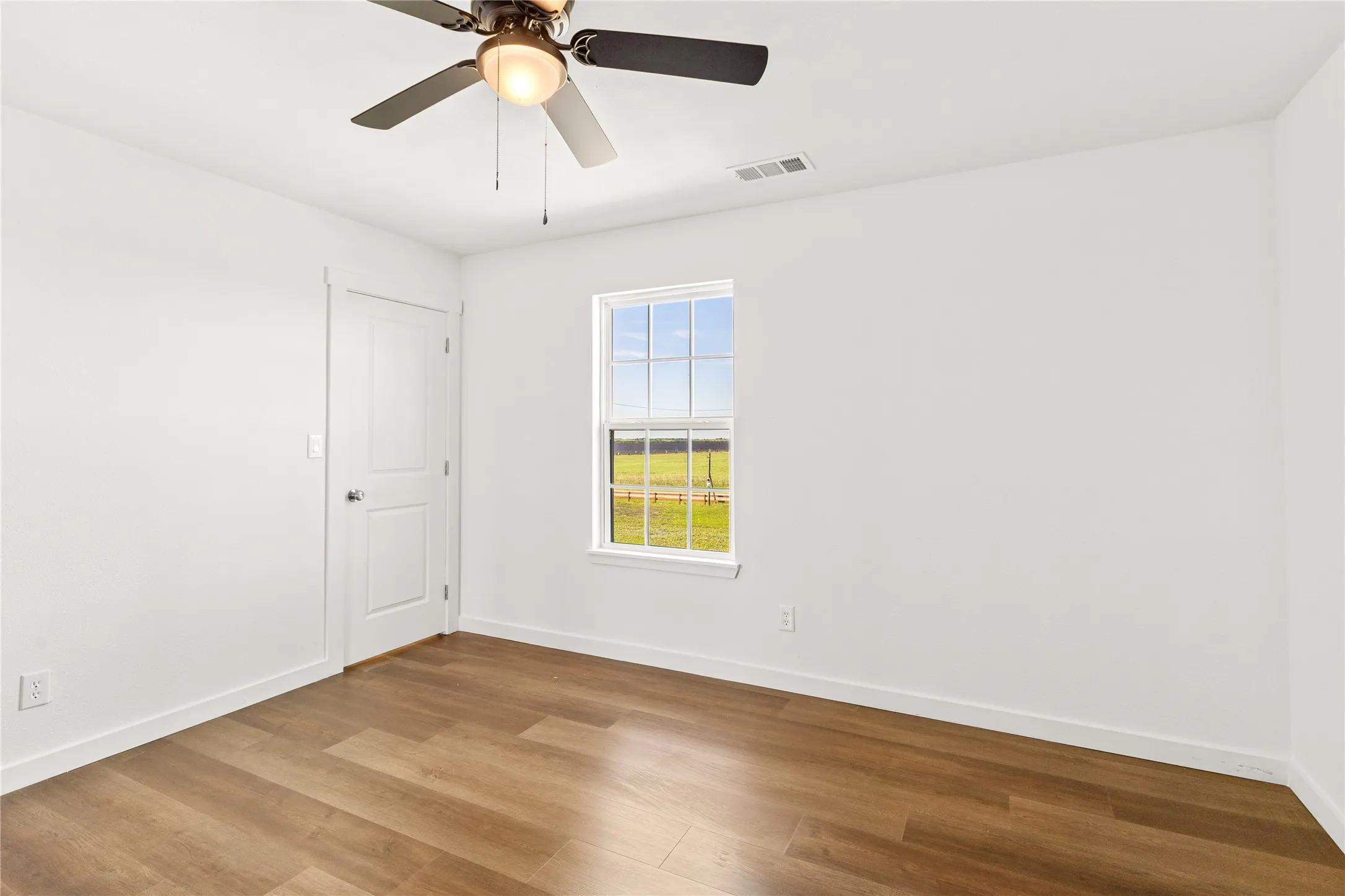 Bright interior space featuring wood-finish flooring, a ceiling fan with integrated lighting, and a window with outdoor scenery