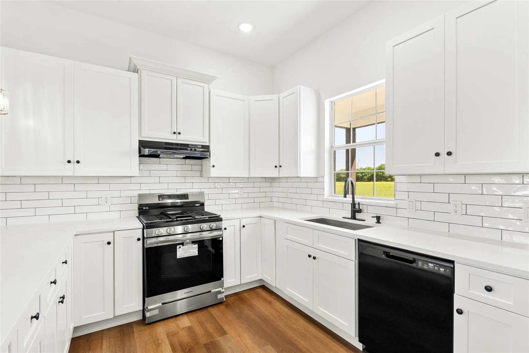 Modern kitchen featuring white shaker cabinetry, stainless steel gas range, black dishwasher, white subway tile backsplash, and wood-finish flooring