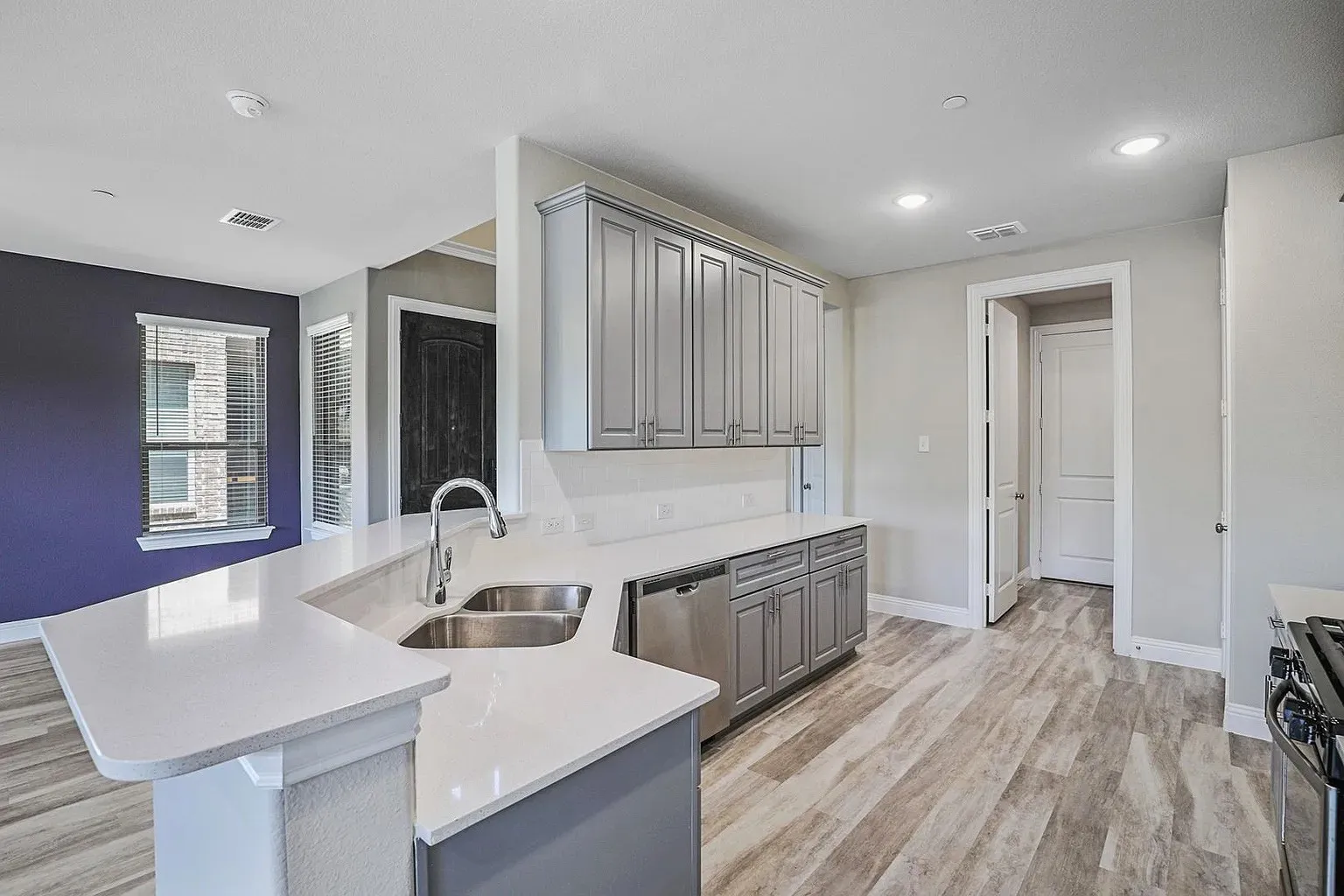 Modern kitchen featuring a dual basin stainless steel sink, stainless steel dishwasher, wood-finish flooring, recessed lighting, and light gray cabinetry with white countertops