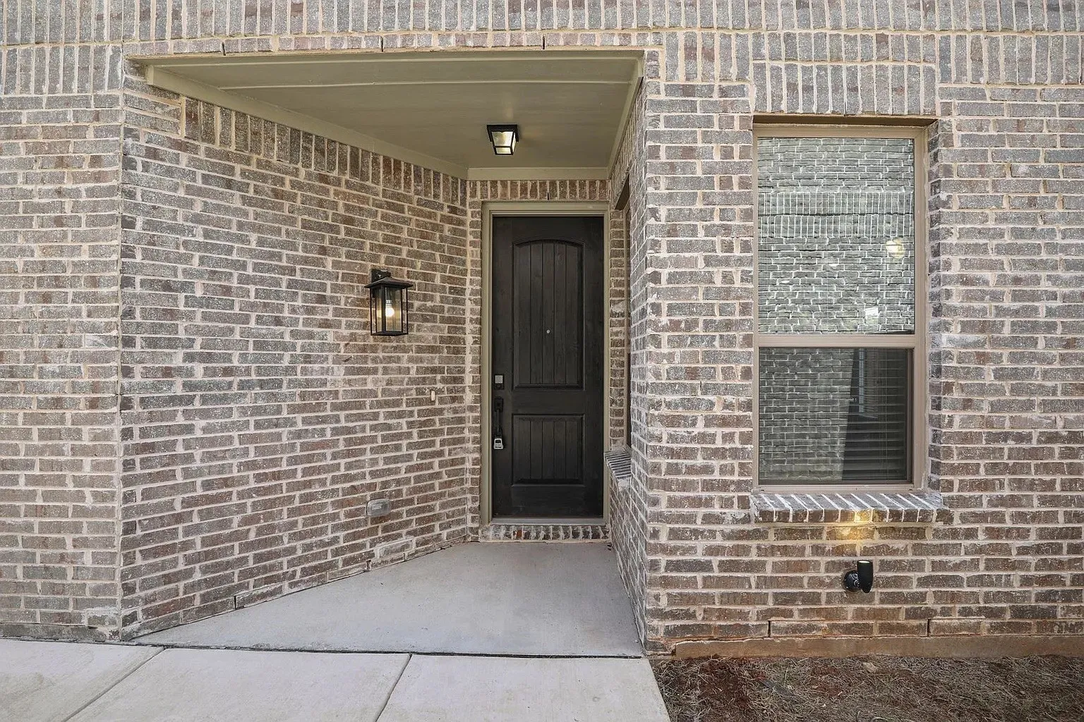 Front entry featuring a dark wood-paneled door, sconce lighting, and a brick exterior facade