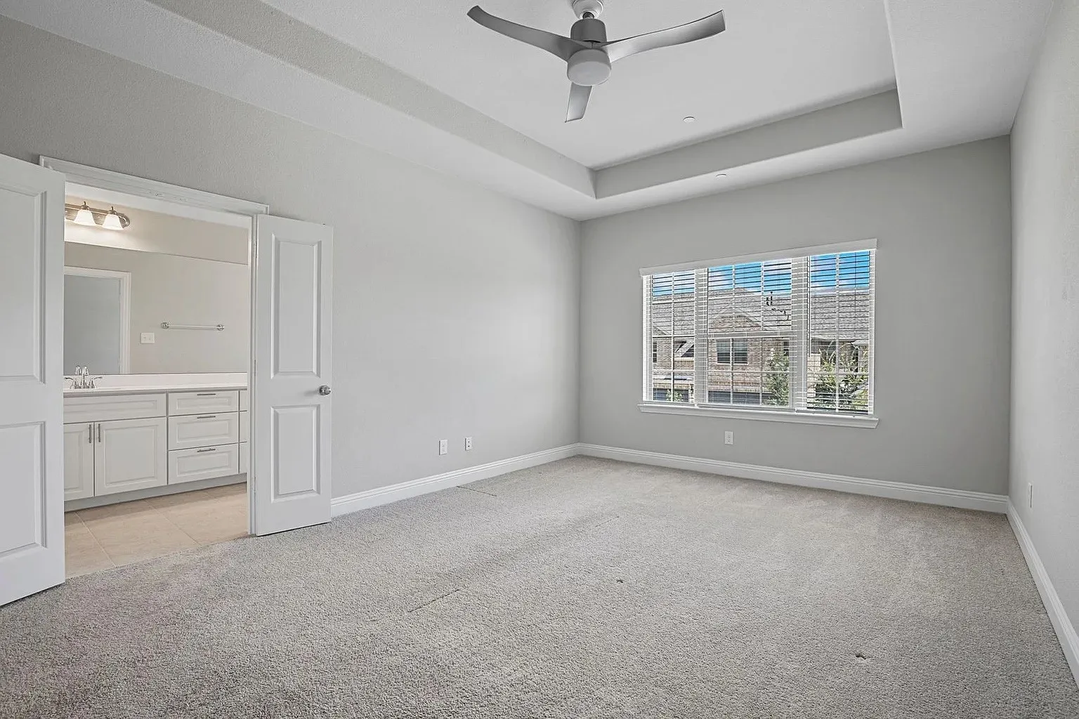 Spacious room featuring light gray walls, plush carpet flooring, and a contemporary ceiling fan