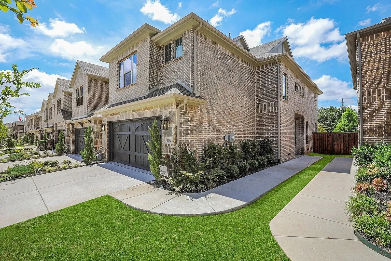 Brick exterior with a dark garage door, concrete driveway, and established landscaping