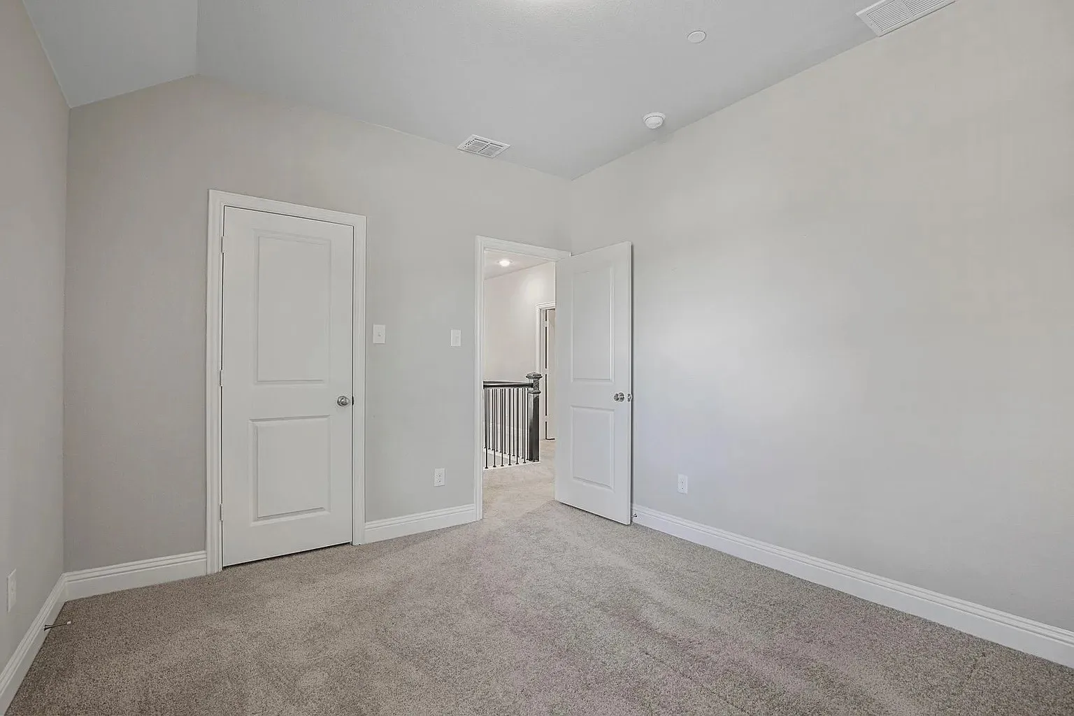 Carpeted interior room featuring light gray walls, white trim, and a vaulted ceiling