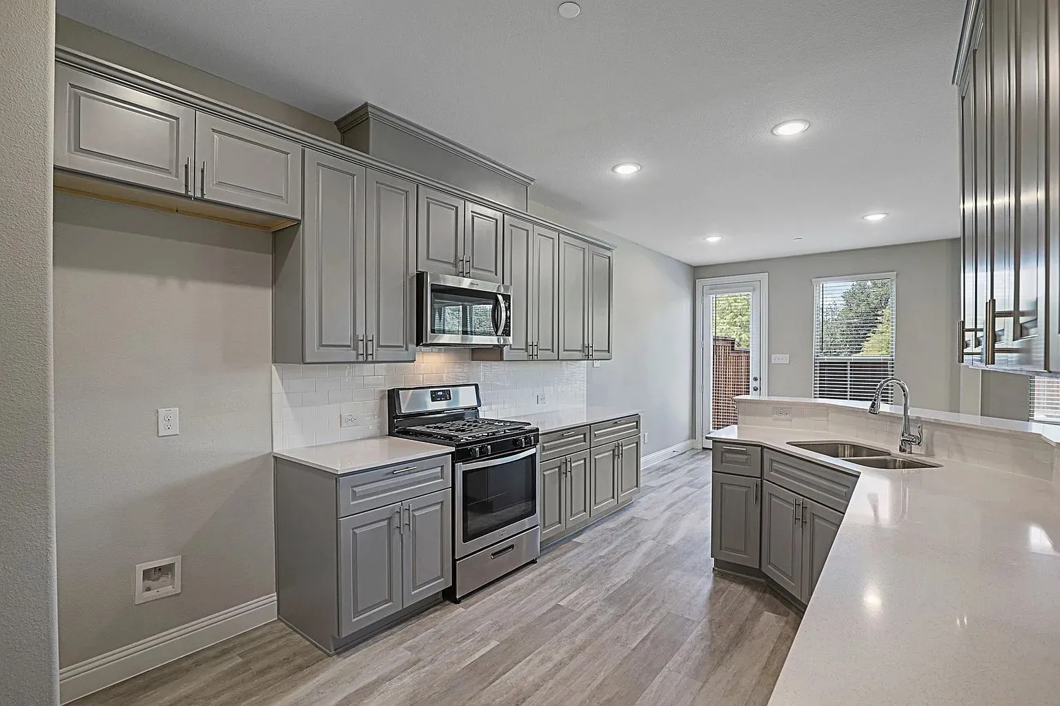 Contemporary kitchen featuring gray shaker cabinetry, stainless steel appliances, a subway tile backsplash, light countertops, and wood-finish flooring