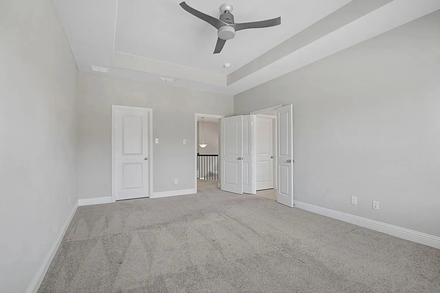 Spacious room featuring light gray carpeting, neutral wall finishes, a modern ceiling fan, and a tray ceiling