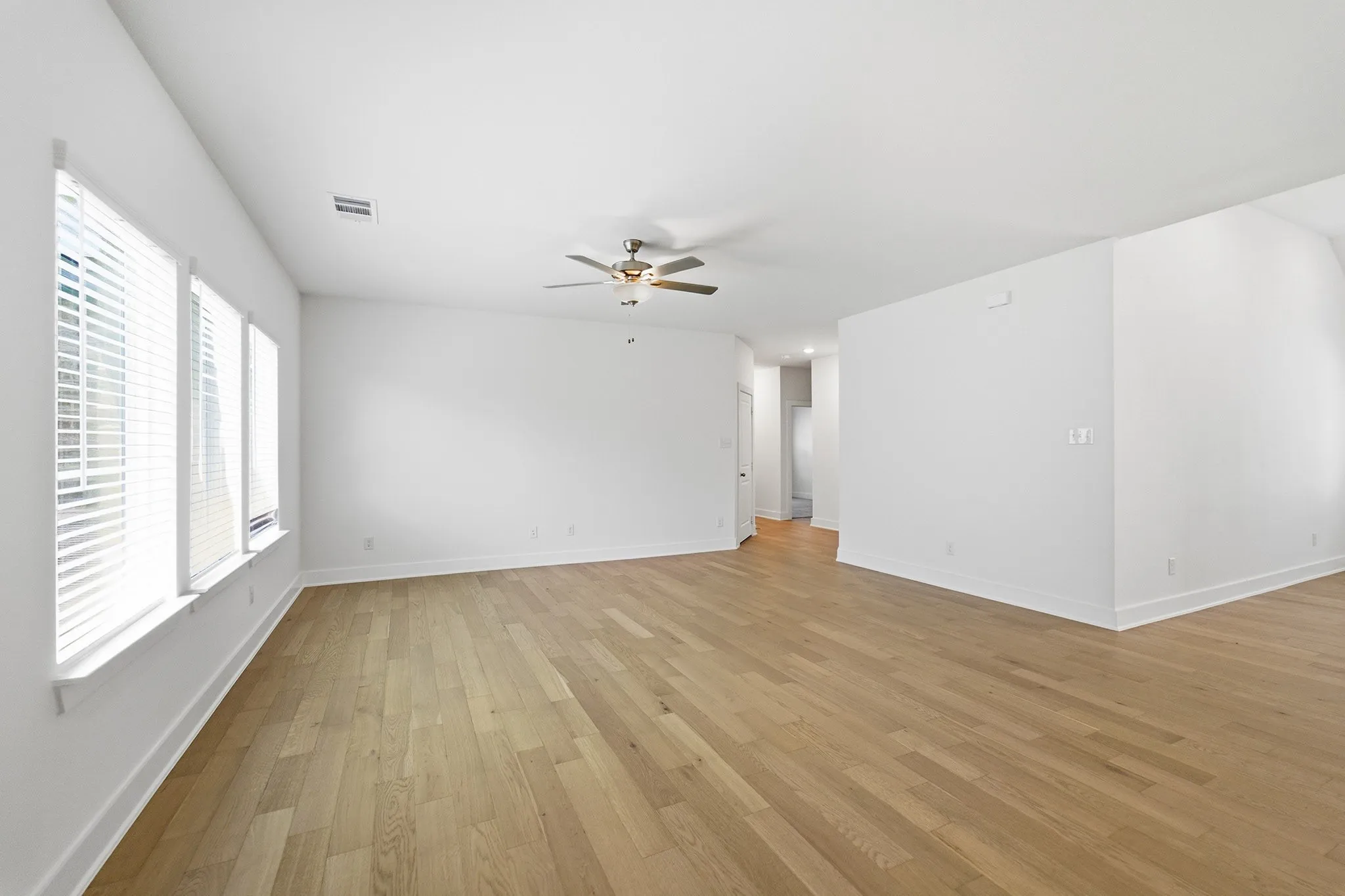 Spacious interior featuring wood-finish flooring, white walls, and bright window treatments