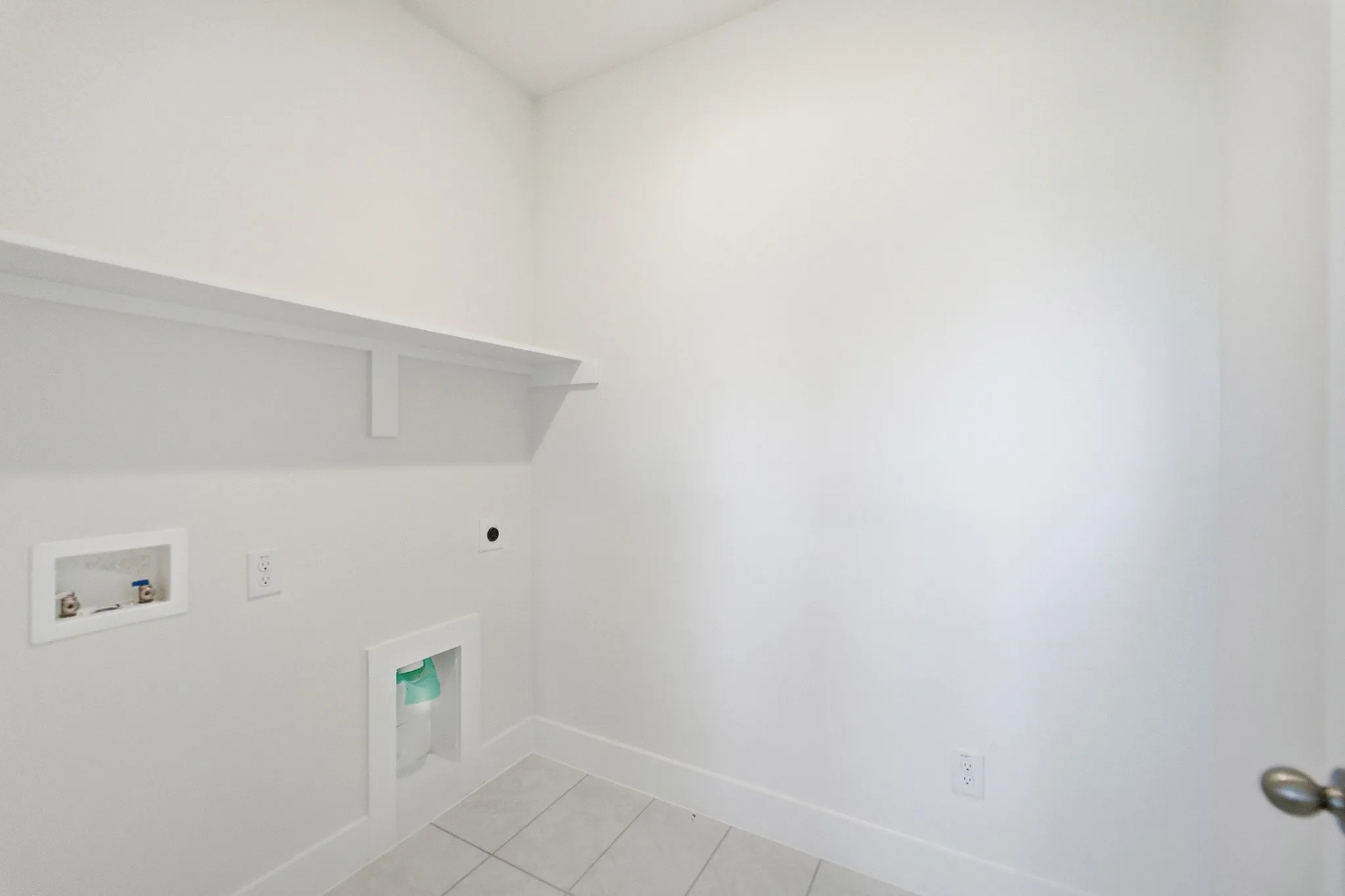 Dedicated laundry area featuring a white storage shelf, utility hookups, and light-toned tile flooring