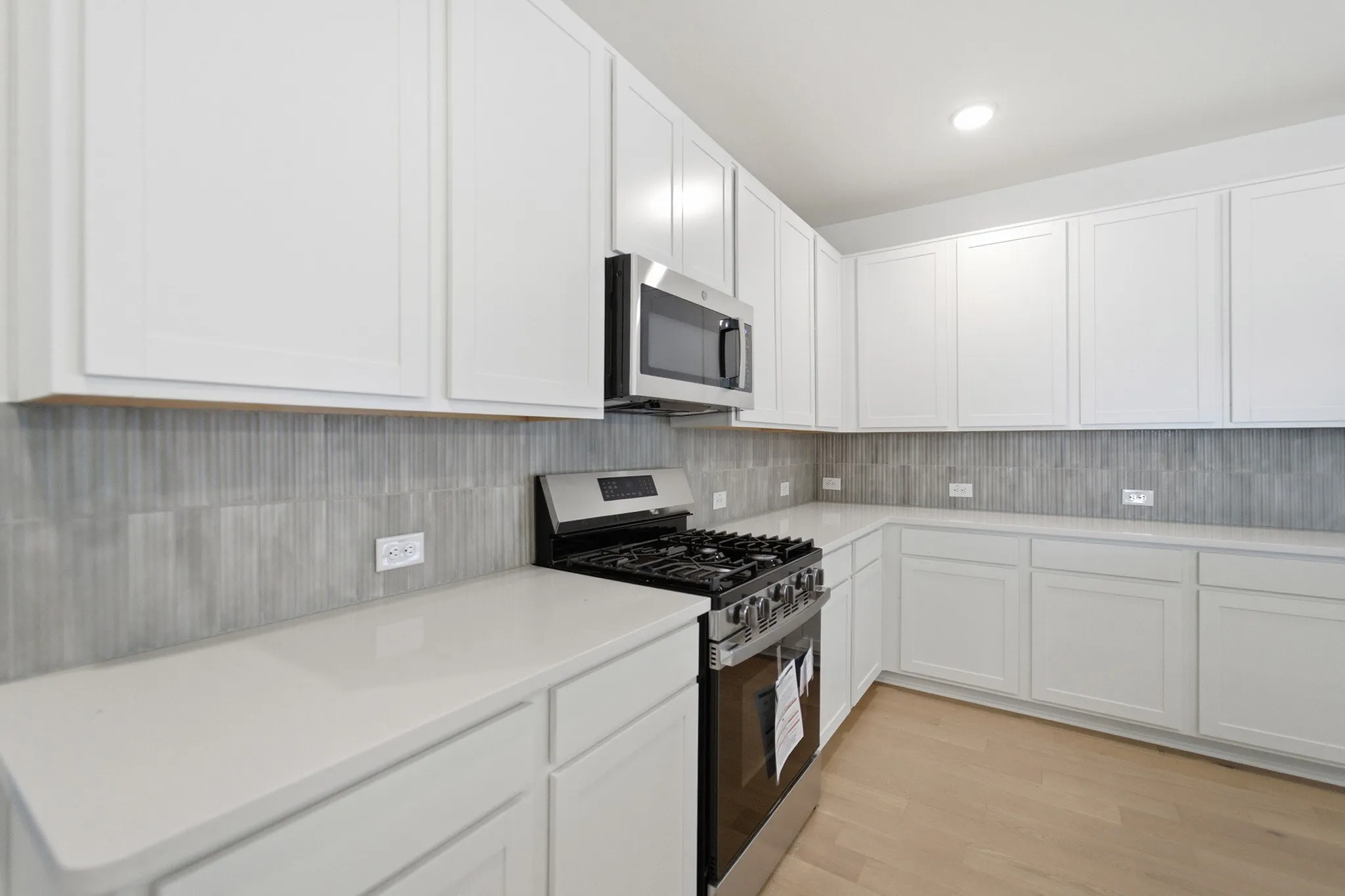 Kitchen featuring white cabinetry, light-toned countertops, a stainless steel gas range, and a coordinating microwave