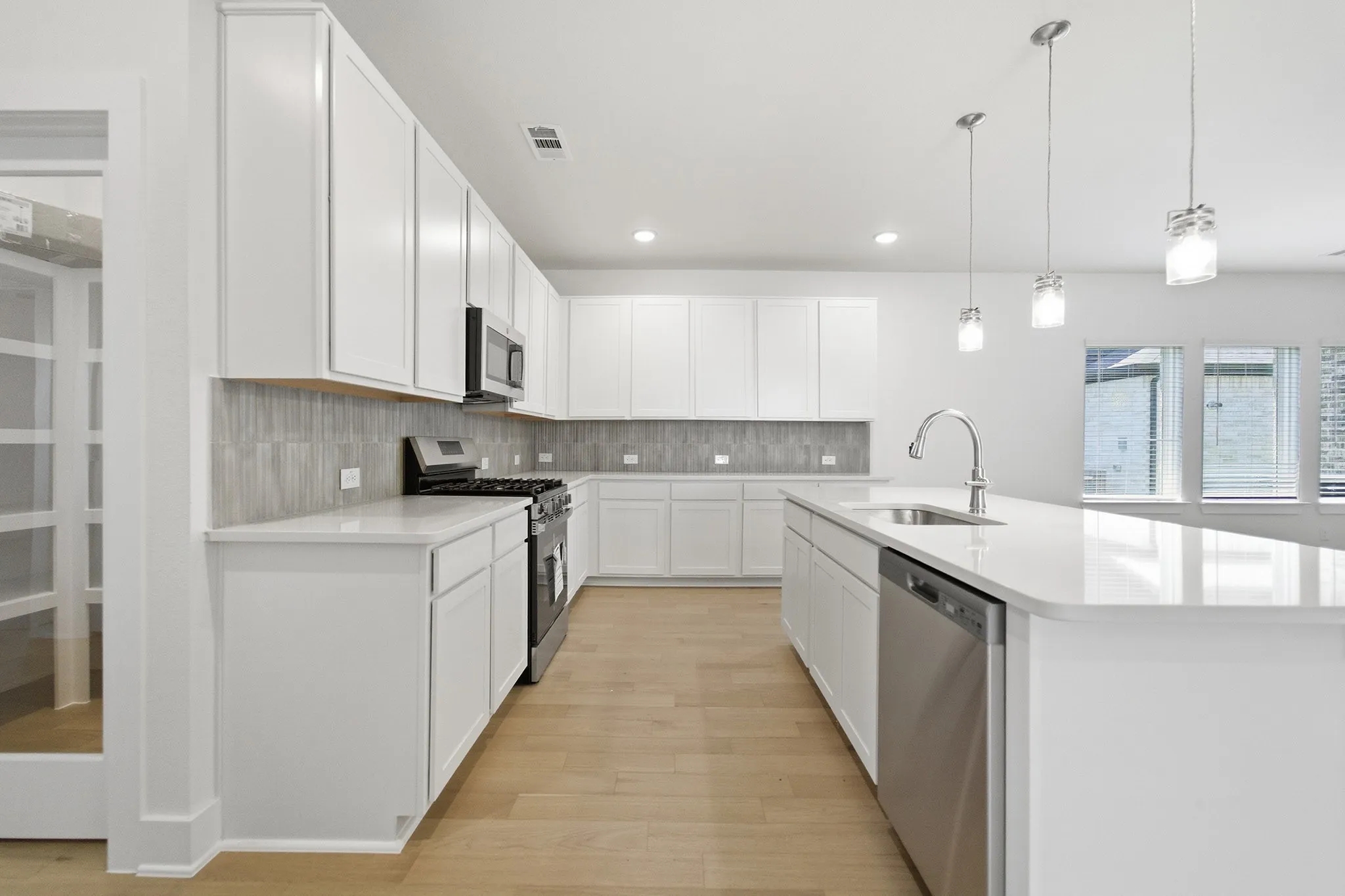 Modern kitchen featuring abundant white cabinetry, stainless steel appliances, light wood-finish flooring, a substantial center island with integrated sink, and an elegant tile backsplash
