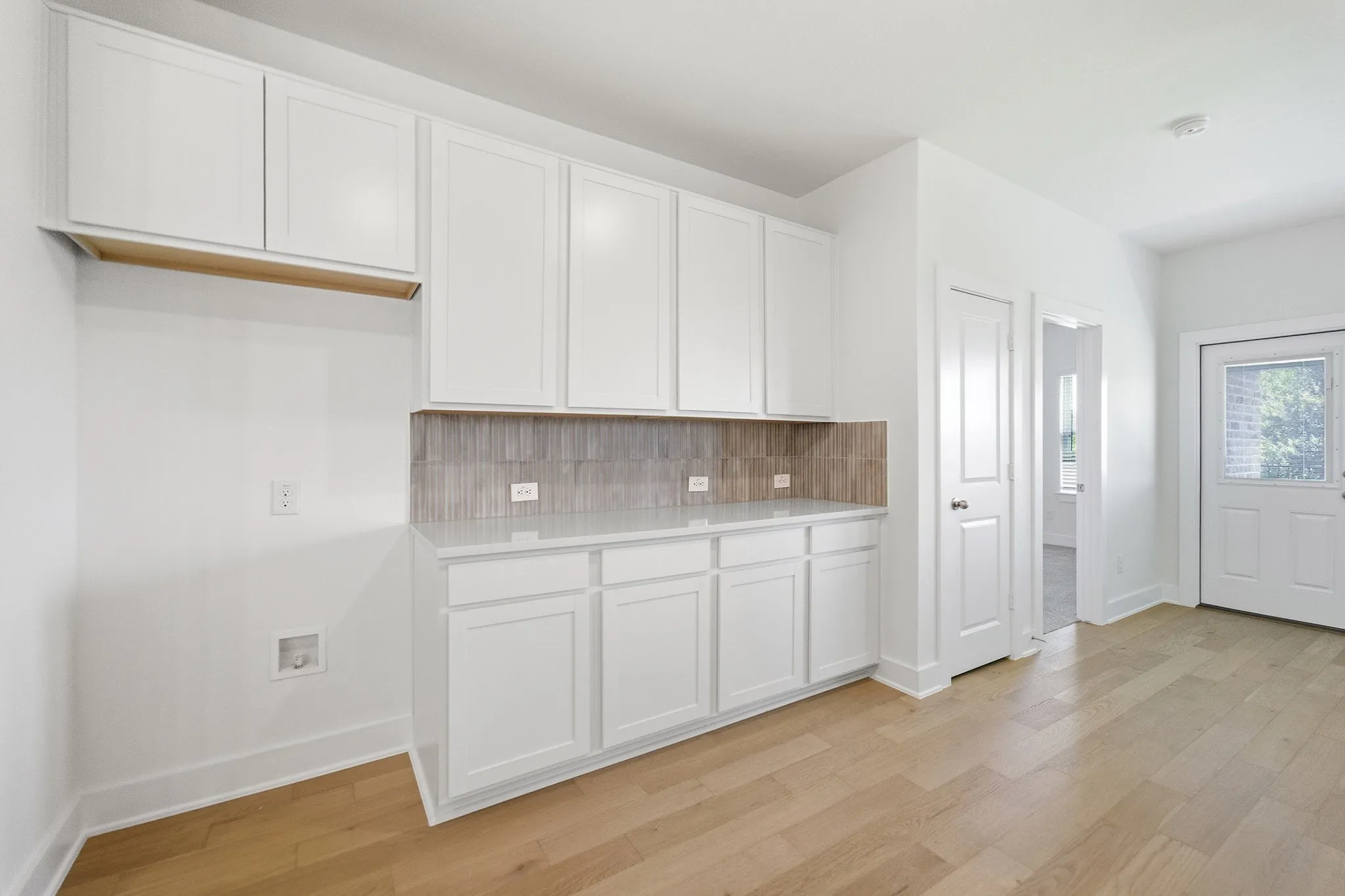 White cabinetry with a light stone-look countertop, tile backsplash, and wood-finish flooring