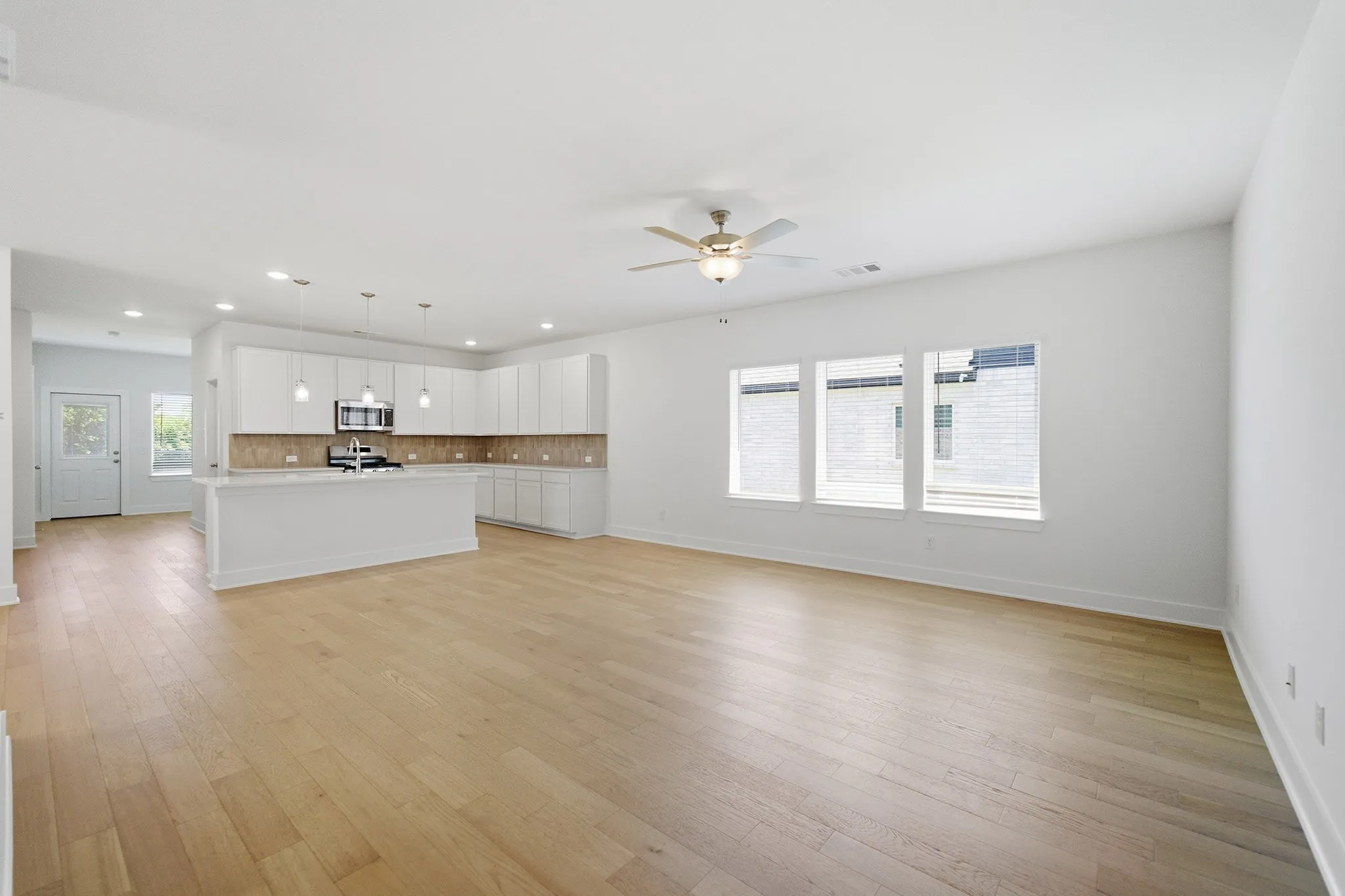 Open-concept living space featuring wood-finish flooring, a contemporary kitchen island with pendant lighting, white cabinetry, and stainless steel appliances