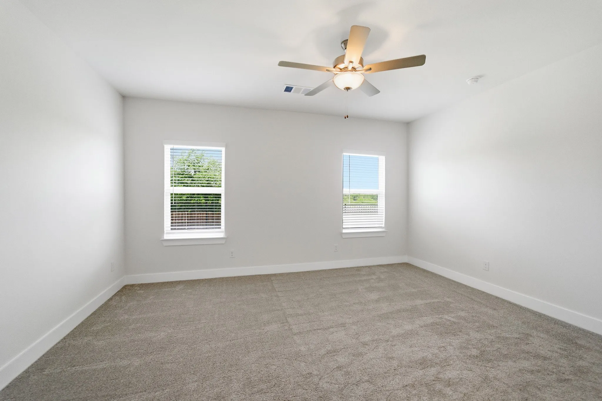 Carpeted room featuring two windows with blinds, a ceiling fan with integrated lighting, white walls, and white baseboards