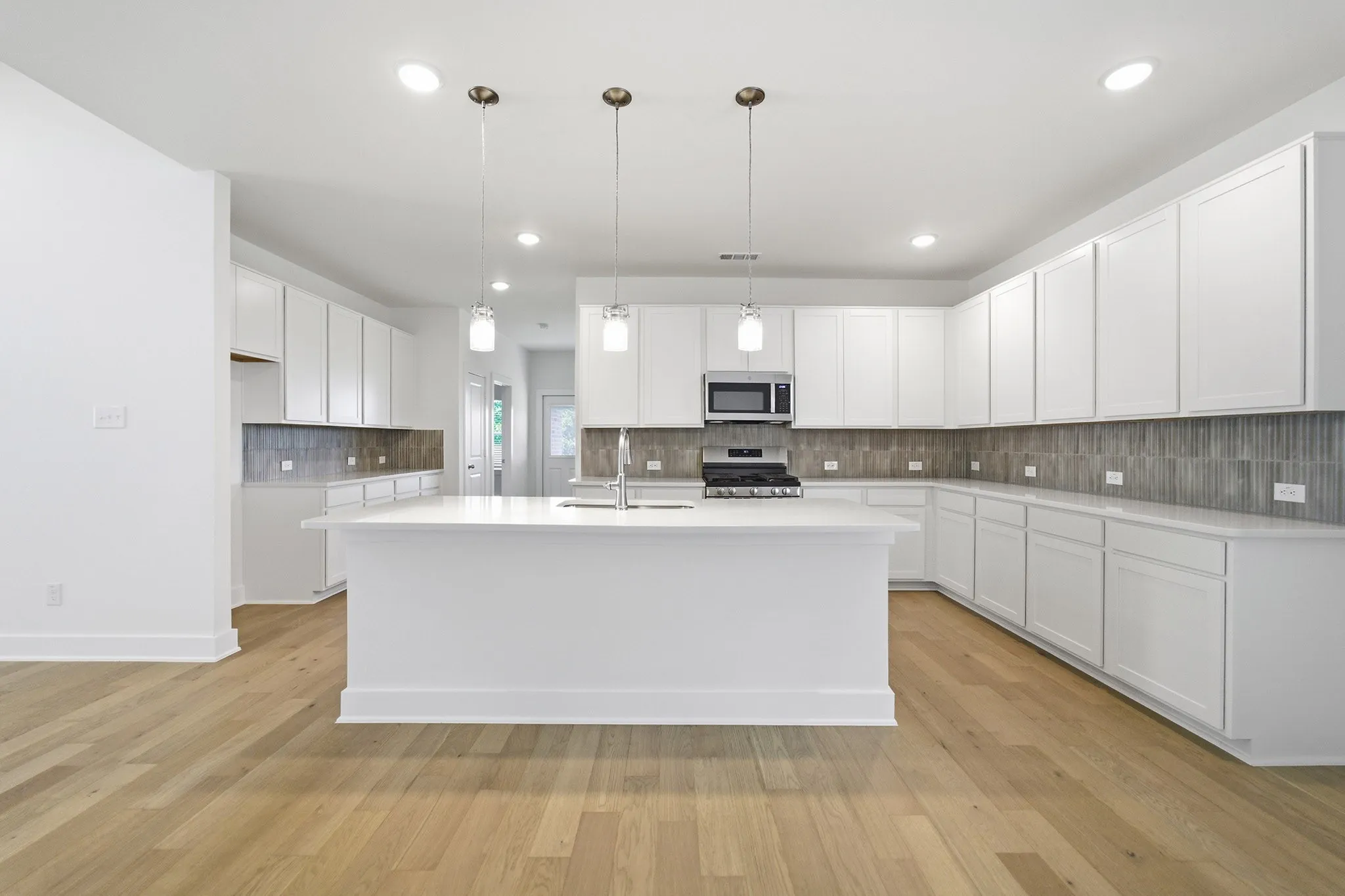 Spacious kitchen featuring an island with a sink, white cabinetry, integrated stainless steel appliances, a gray tiled backsplash, and wood-finish flooring