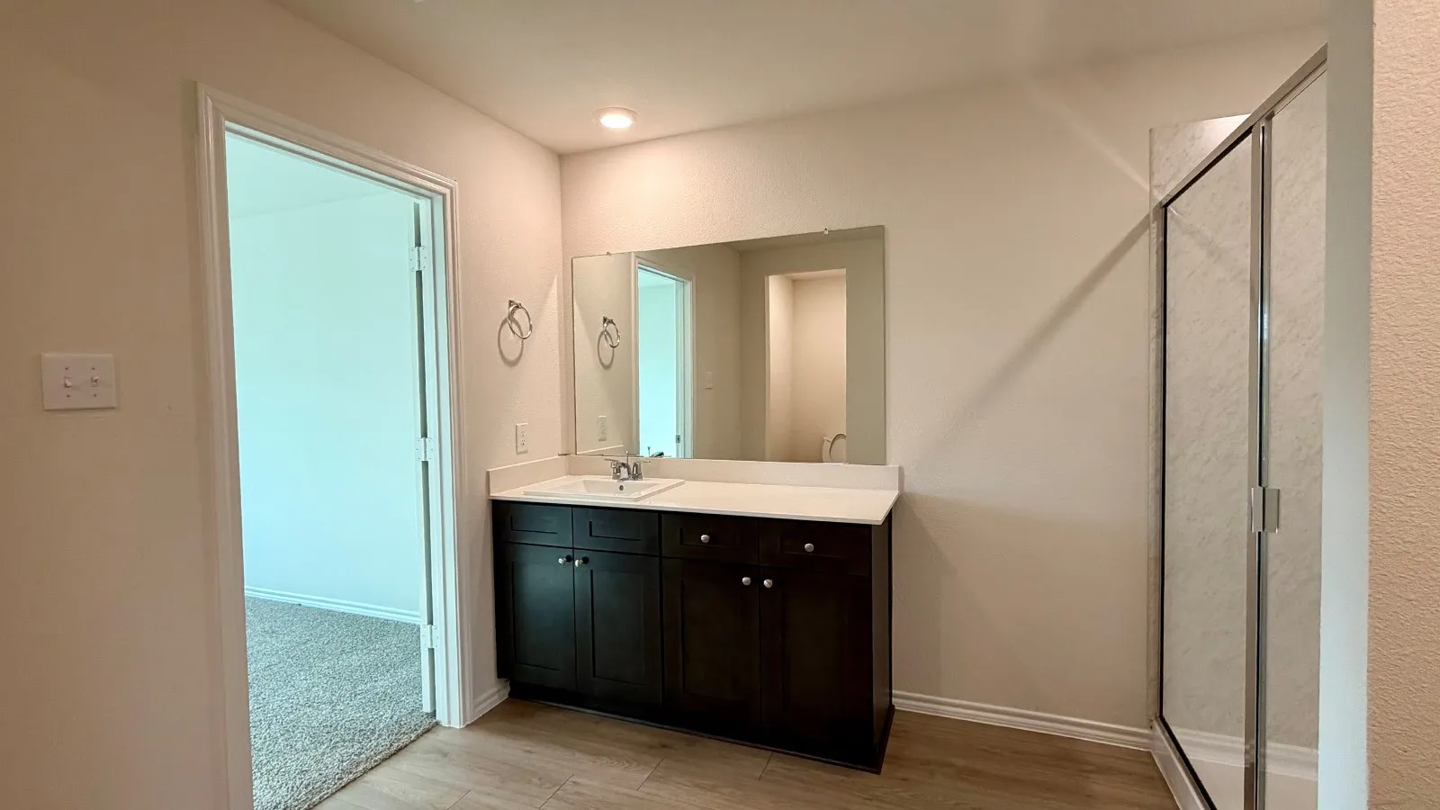 Bathroom featuring a dark wood-finish vanity with a white countertop and integrated sink, a large wall-mounted mirror, recessed lighting, and wood-finish flooring