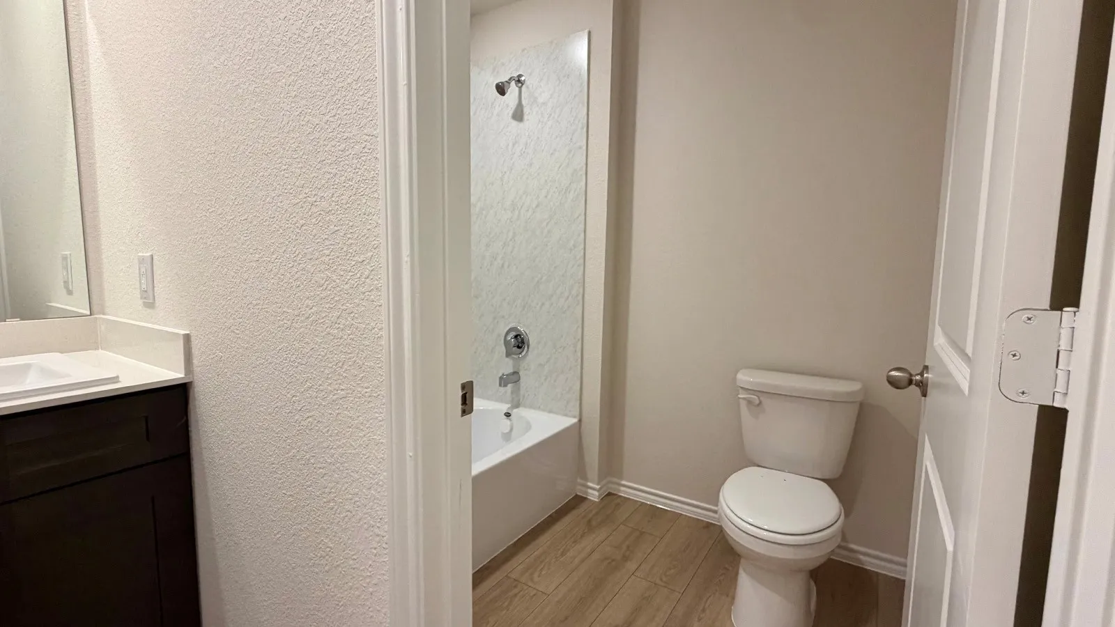 Contemporary bathroom featuring a white ceramic toilet with elongated bowl, wood-finish flooring, and a frameless glass-enclosed shower alcove with white subway tile surround