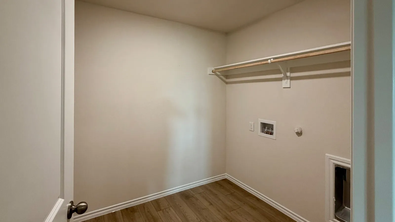 Laundry area featuring wood-finish flooring, light-toned walls, and a built-in hanging rod with shelving