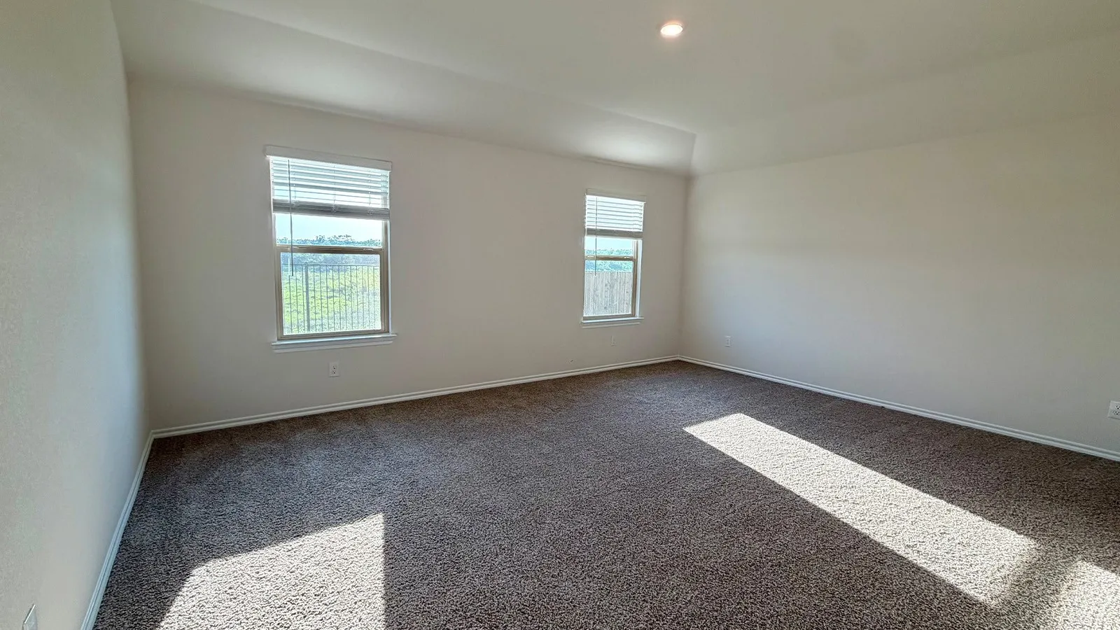 Spacious interior room featuring two windows with blinds, tray ceiling, recessed lighting, and textured carpet flooring